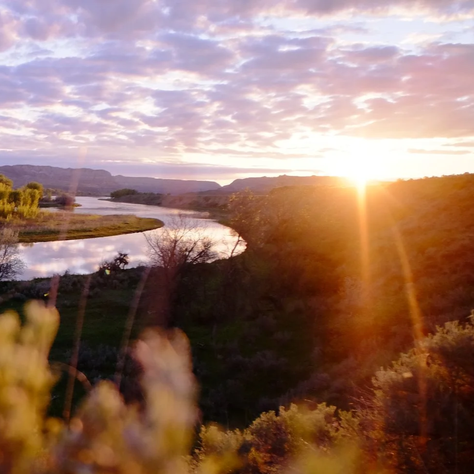 Sunset over a river with mountains in the background and clouds in the sky.