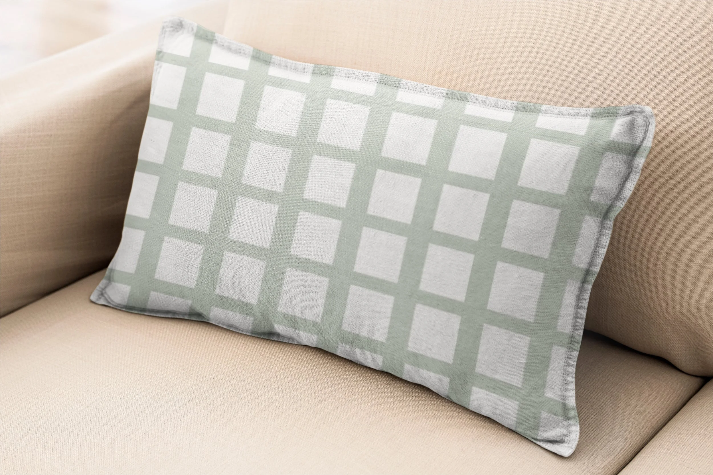Soft sage green and cream grid lumbar pillow styled on a warm neutral sofa.