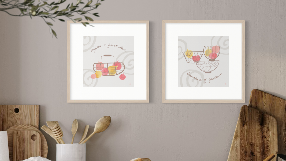 Two framed Quiet Spaces illustrations in soft peach, pink and yellow displayed together on a warm neutral kitchen wall.