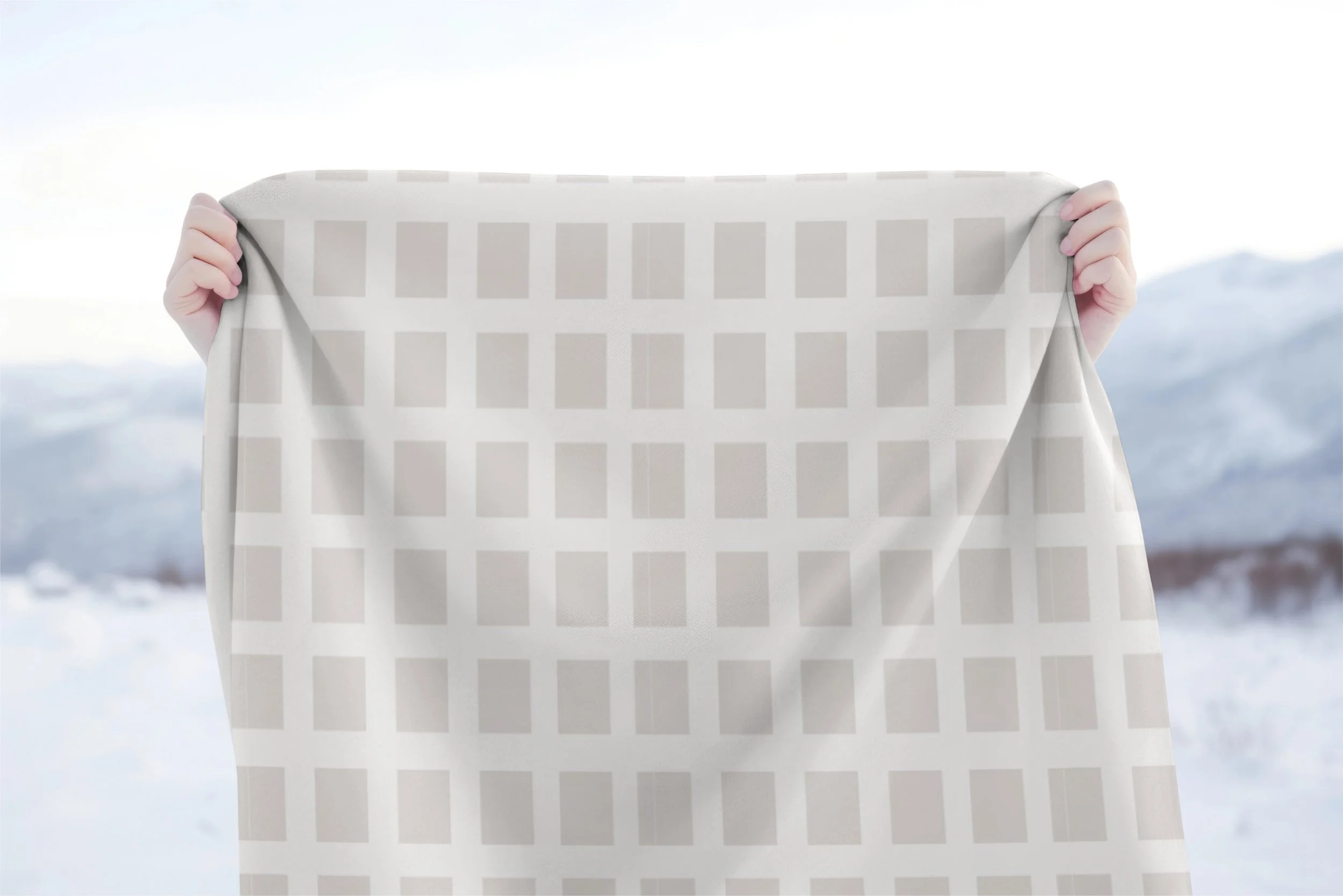 Soft cream throw blanket with a large taupe square pattern held against a snowy mountain backdrop.