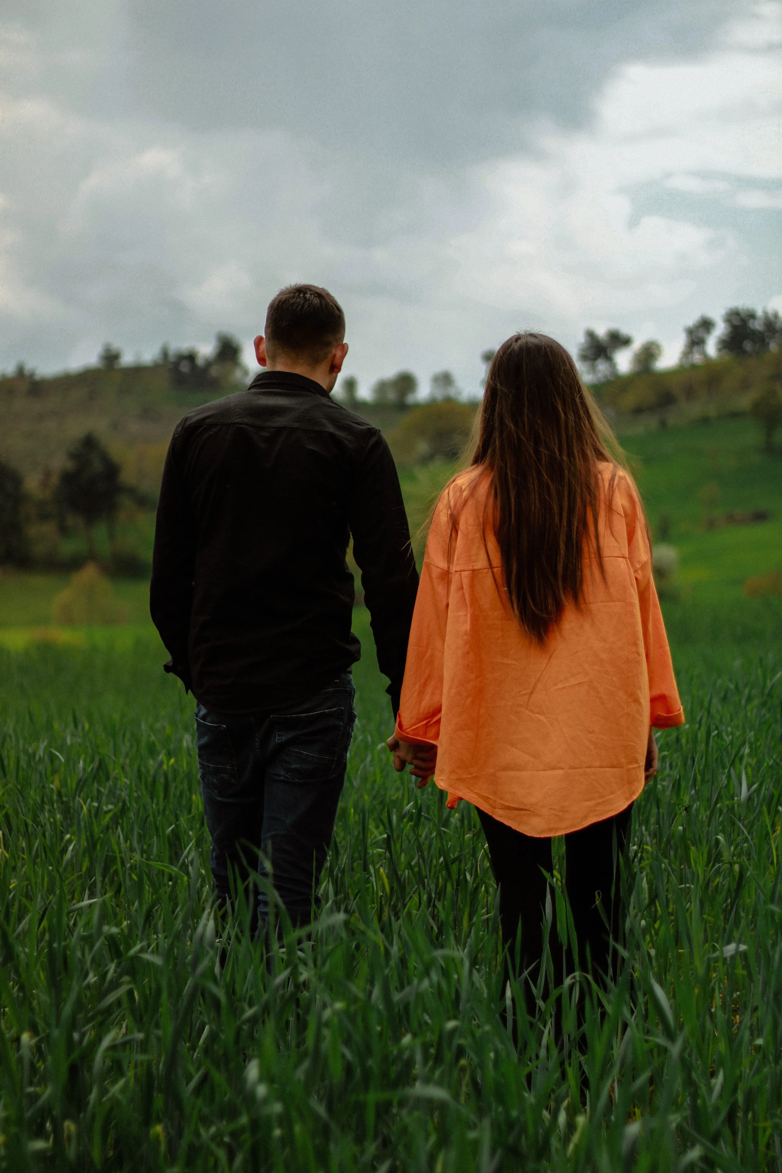 couple walking through a grassy field holding hands