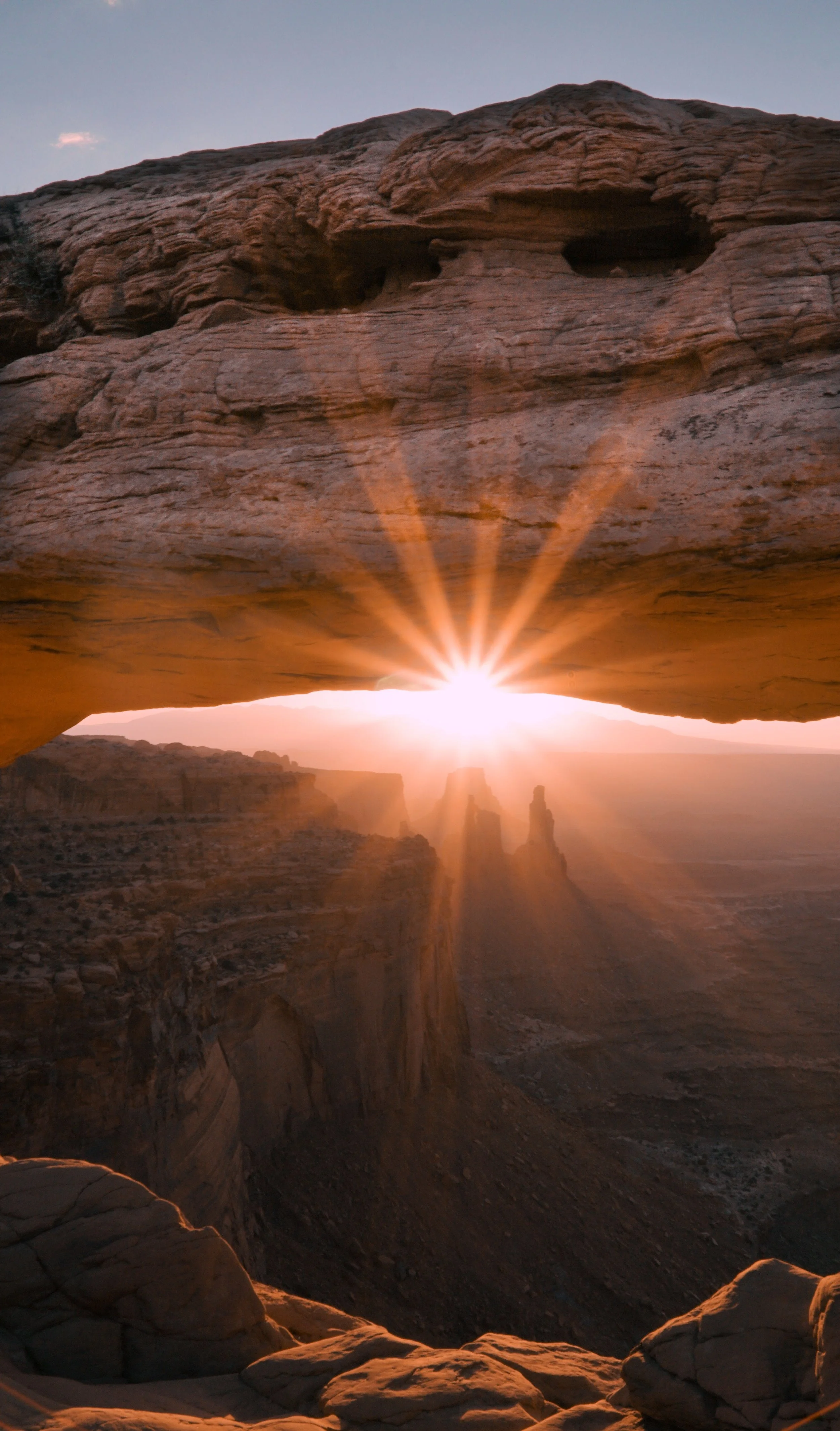Sunset view through the arch of the Grand Canyon, with sunlight shining through the rock formation, highlighting the canyon's layered cliffs and formations.