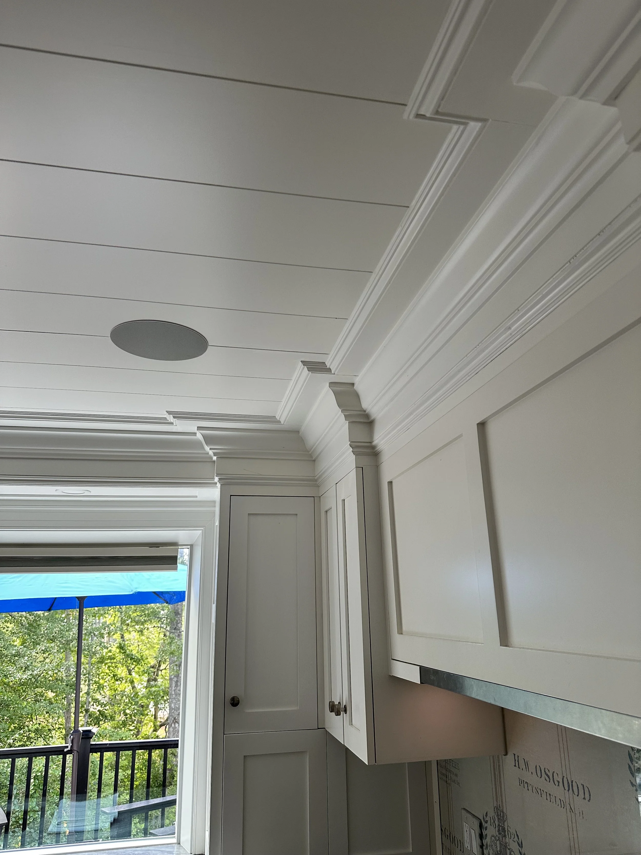 Interior view of a kitchen with white cabinetry and crown molding, a sliding glass door leading to a balcony, and trees outside.
