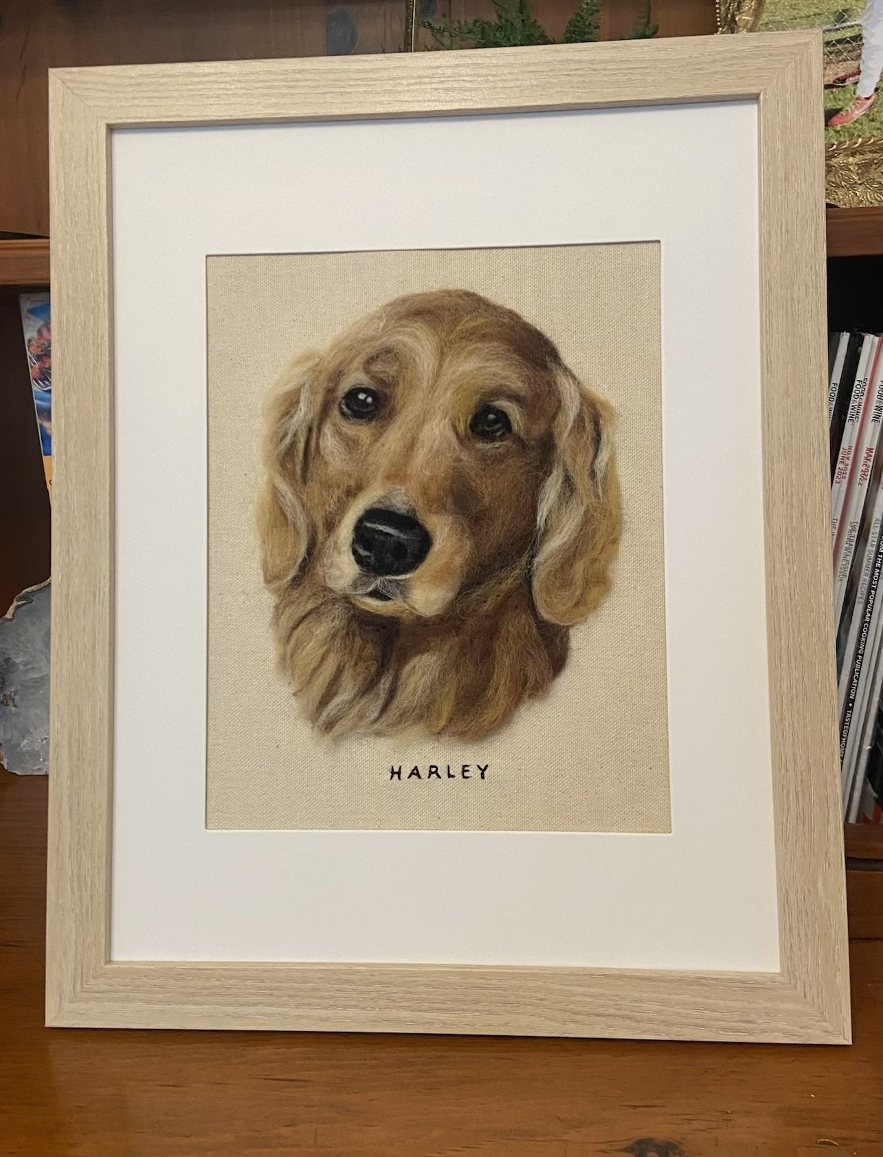 A framed artwork of a realistic painting of a golden retriever dog named Harley, with detailed fur and expressive eyes, on a light-colored canvas. The dog's name, 'HARLEY,' is written below the portrait.