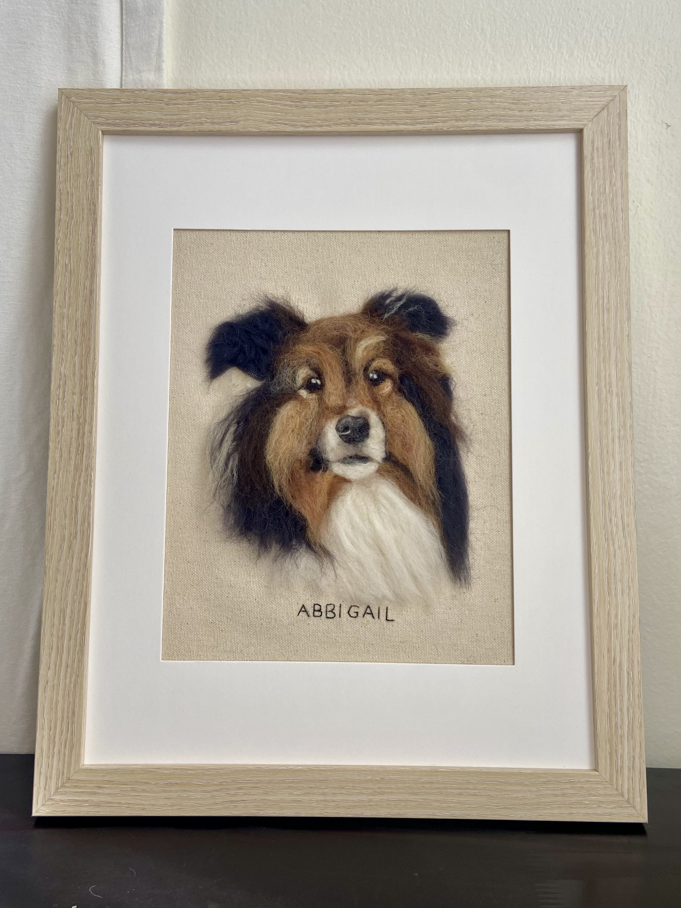 Framed needlework or embroidery of a dog with the name 'ABIGAIL' stitched below.