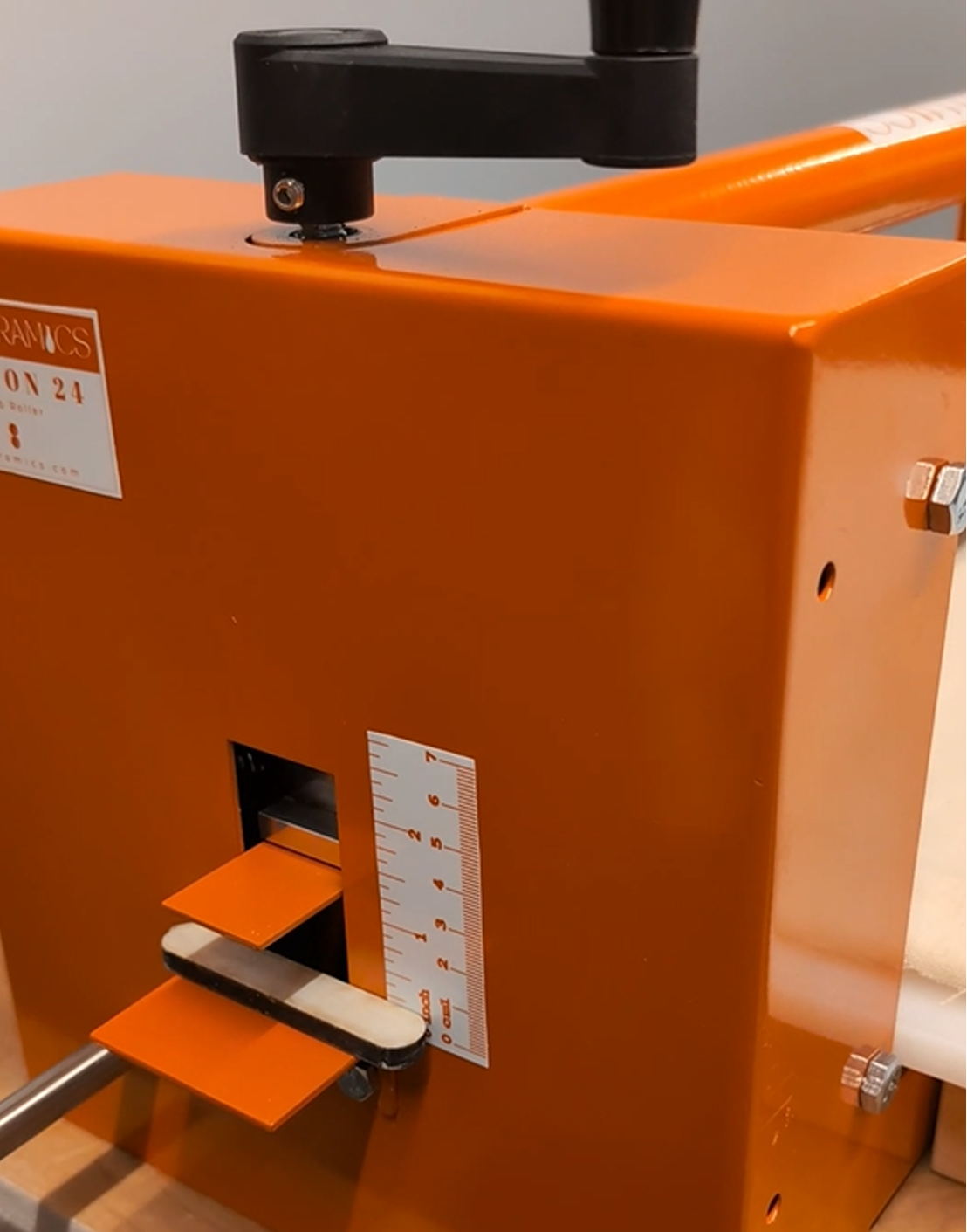 An orange laboratory or industrial device with a sliding mechanism, a ruler display, and a black top component.