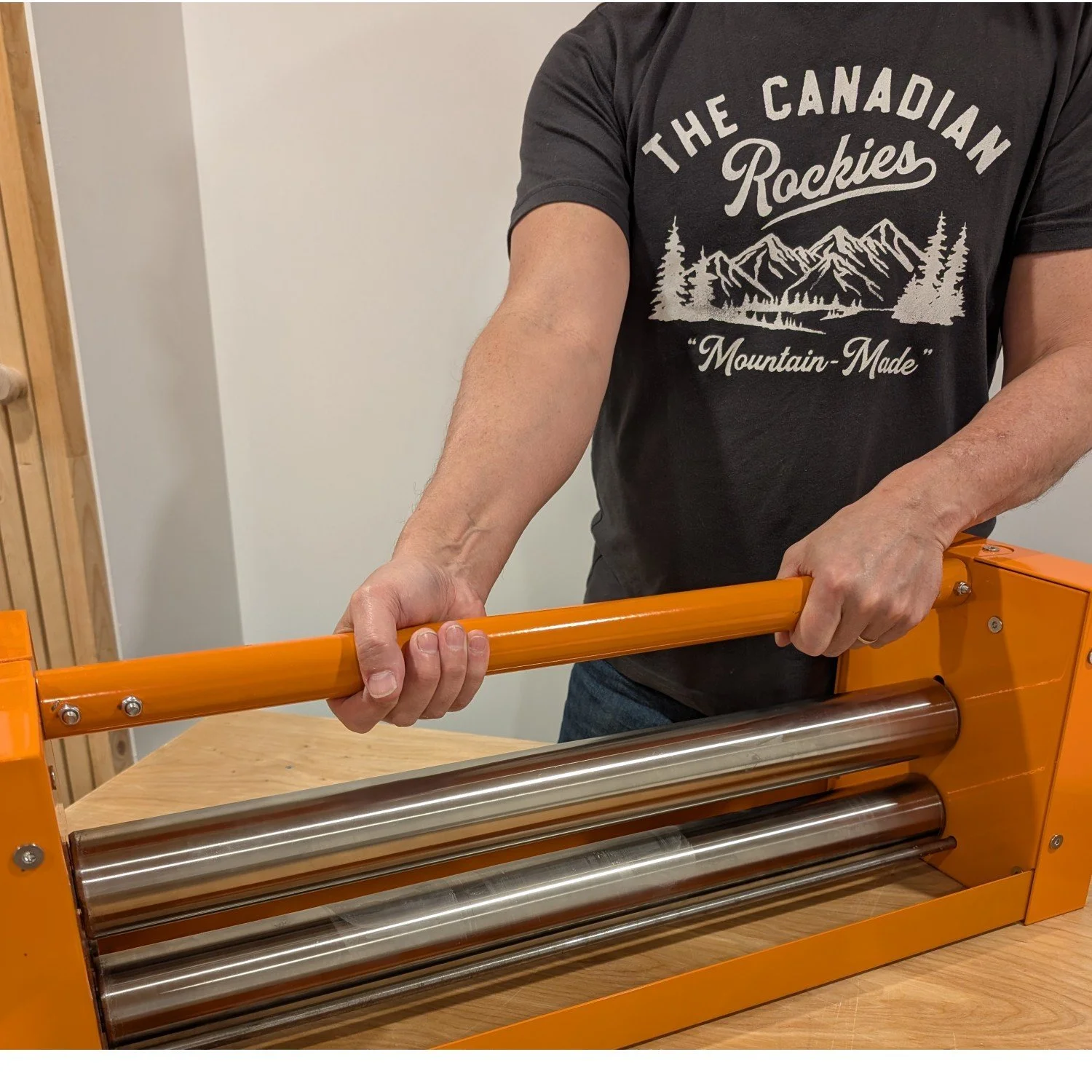 Person operating an orange pasta machine, rolling dough on a wooden table.