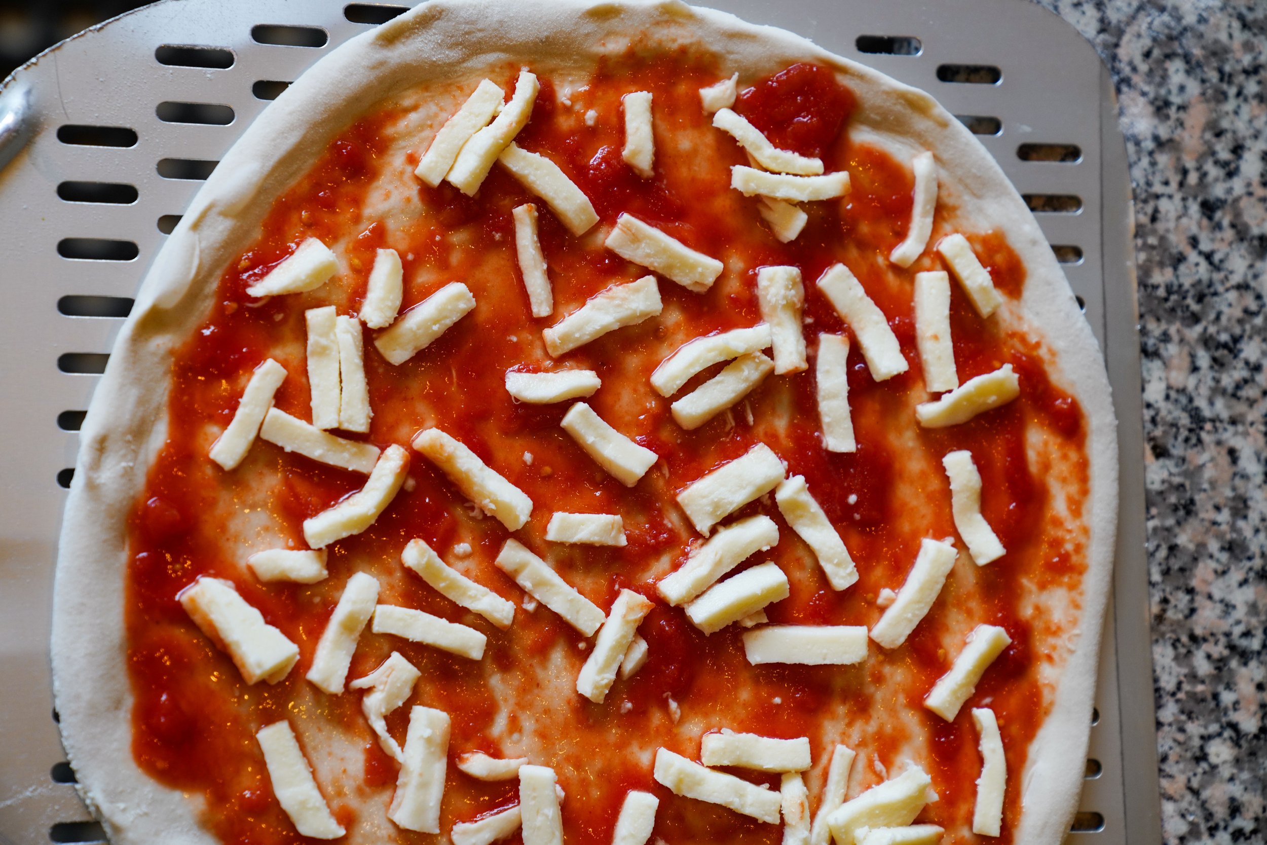Unbaked pizza with tomato sauce and shredded cheese on a pizza crust, sitting on a baking sheet with a granite countertop in the background.