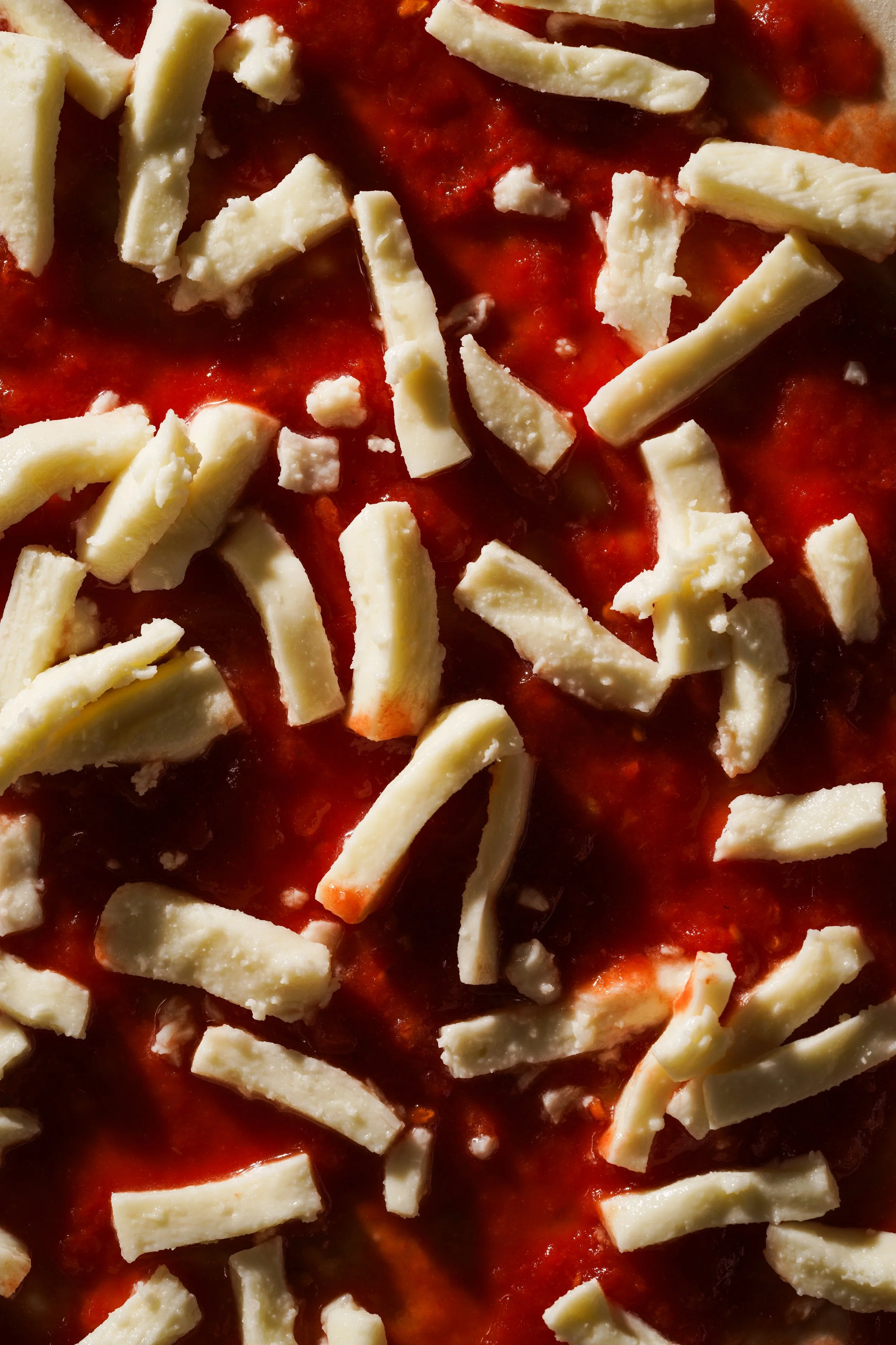 Close-up of shredded mozzarella cheese on a pizza with tomato sauce.