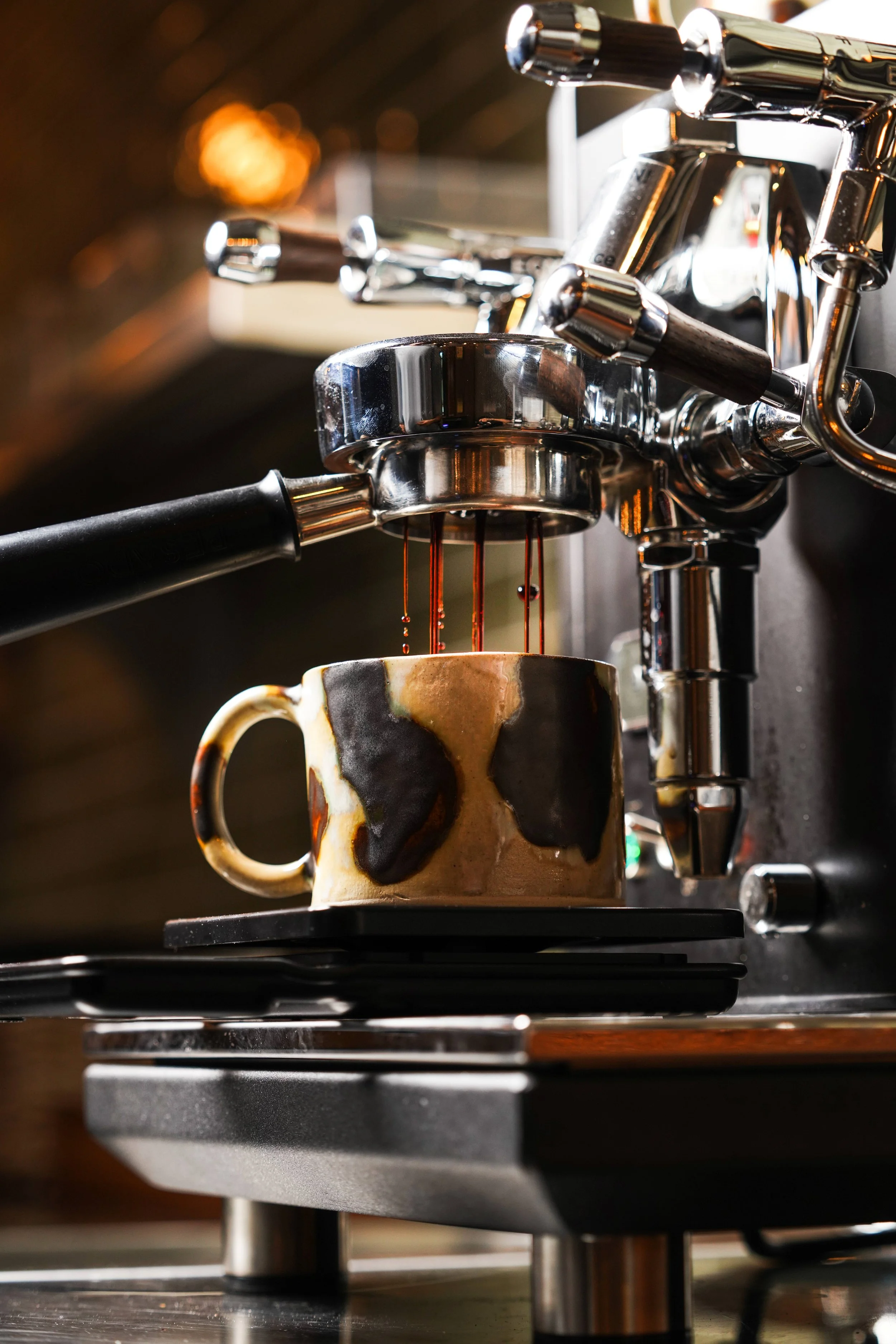 A close-up of a coffee machine pouring coffee into a ceramic mug, with a dark background and warm lighting.