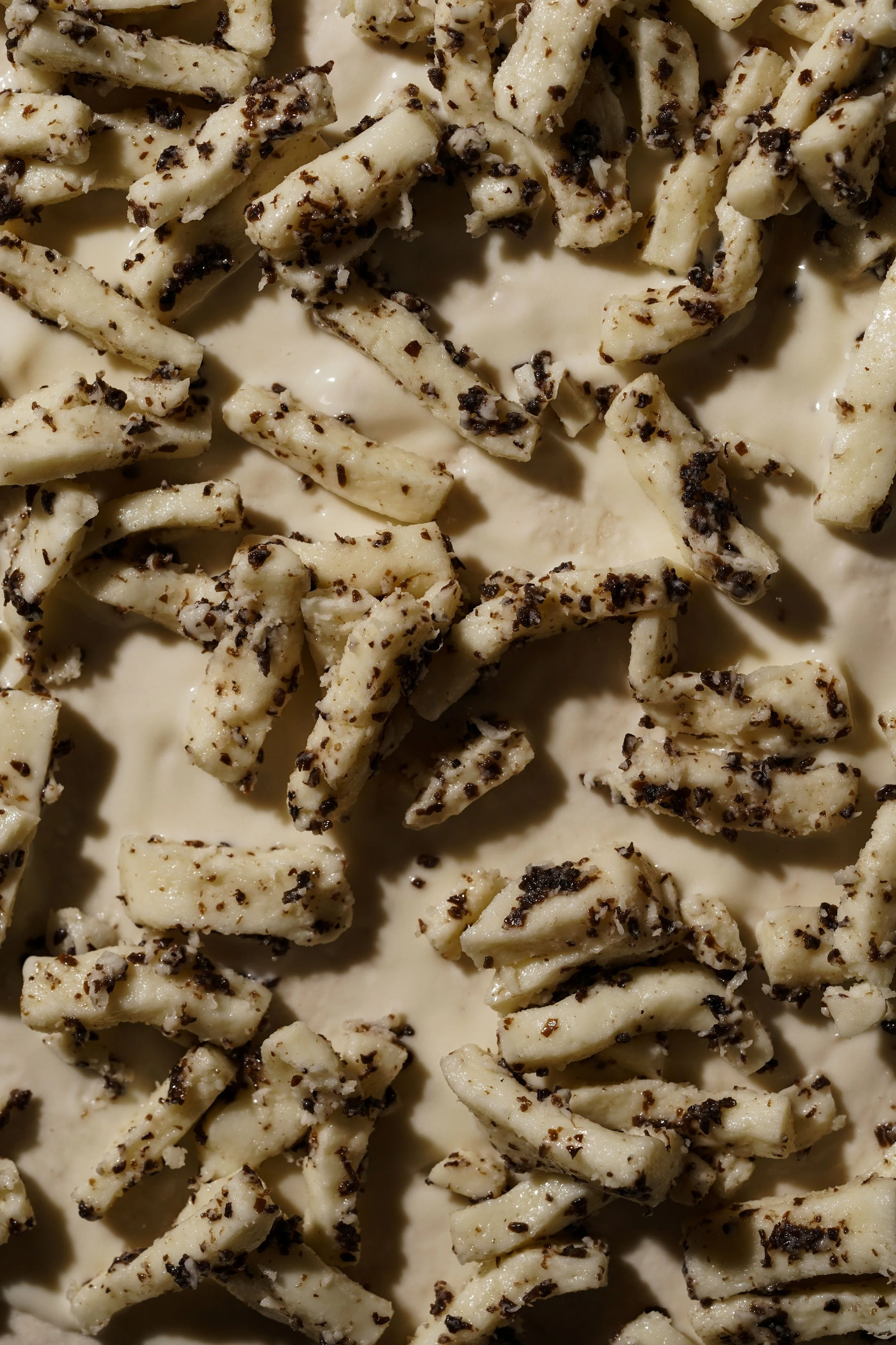 Close-up of white chocolate pieces covered with crushed black pepper and black pepper flakes on a creamy surface.