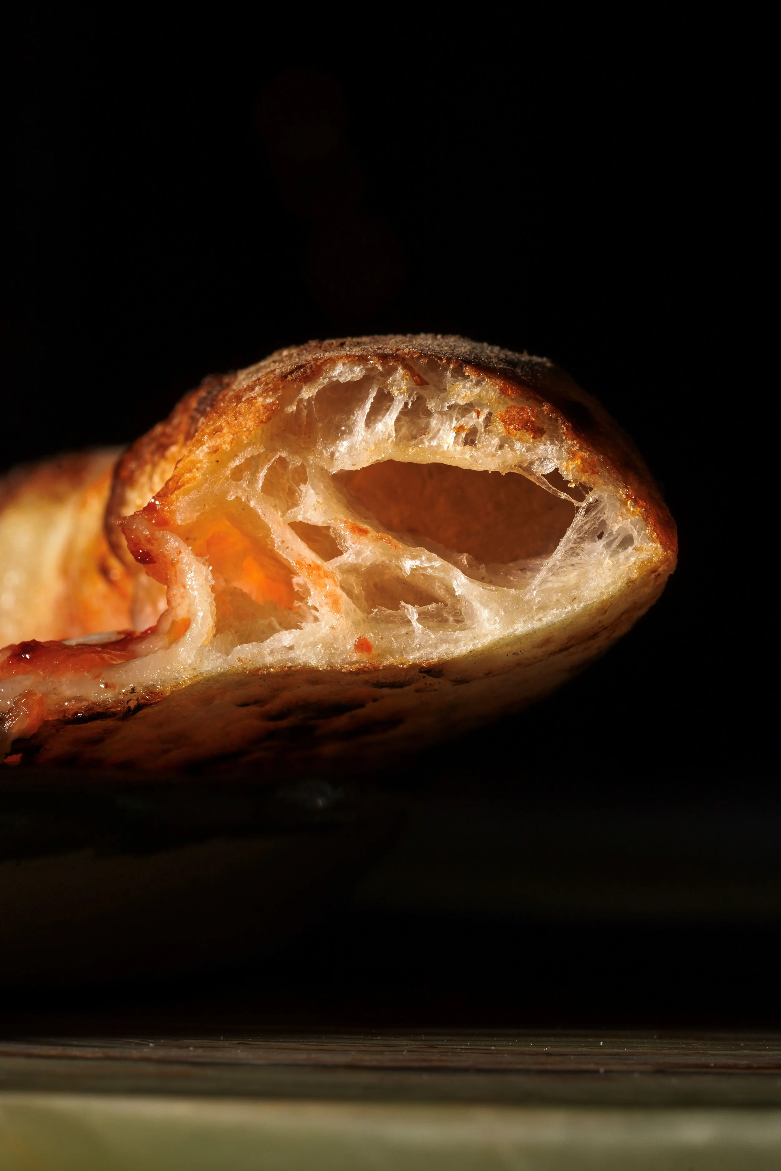 Close-up of a partially eaten baked bread roll, showing its airy, fluffy interior and golden crust against a dark background.