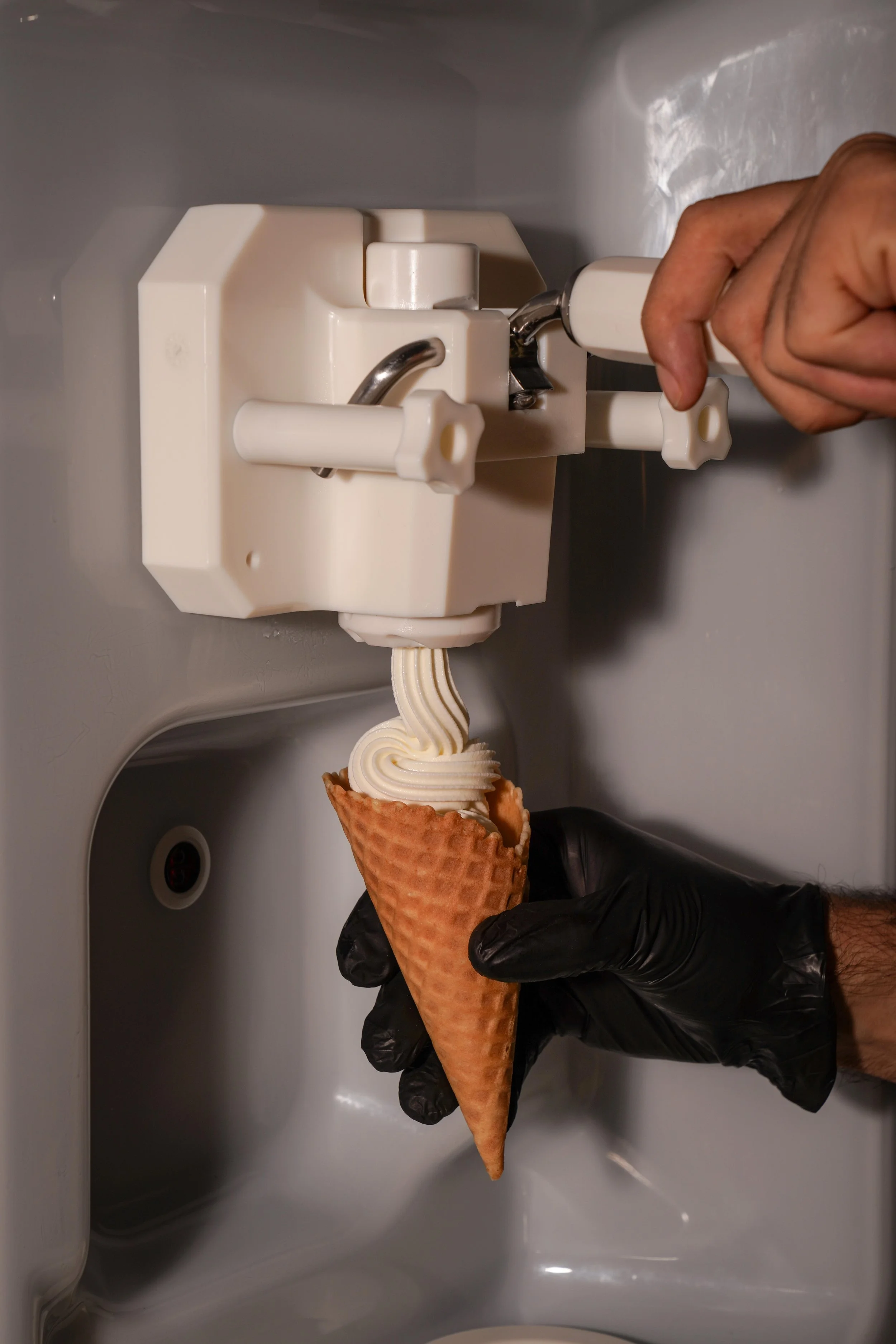 A person's hand in a black glove is placing a cone filled with soft serve ice cream into a vending machine.