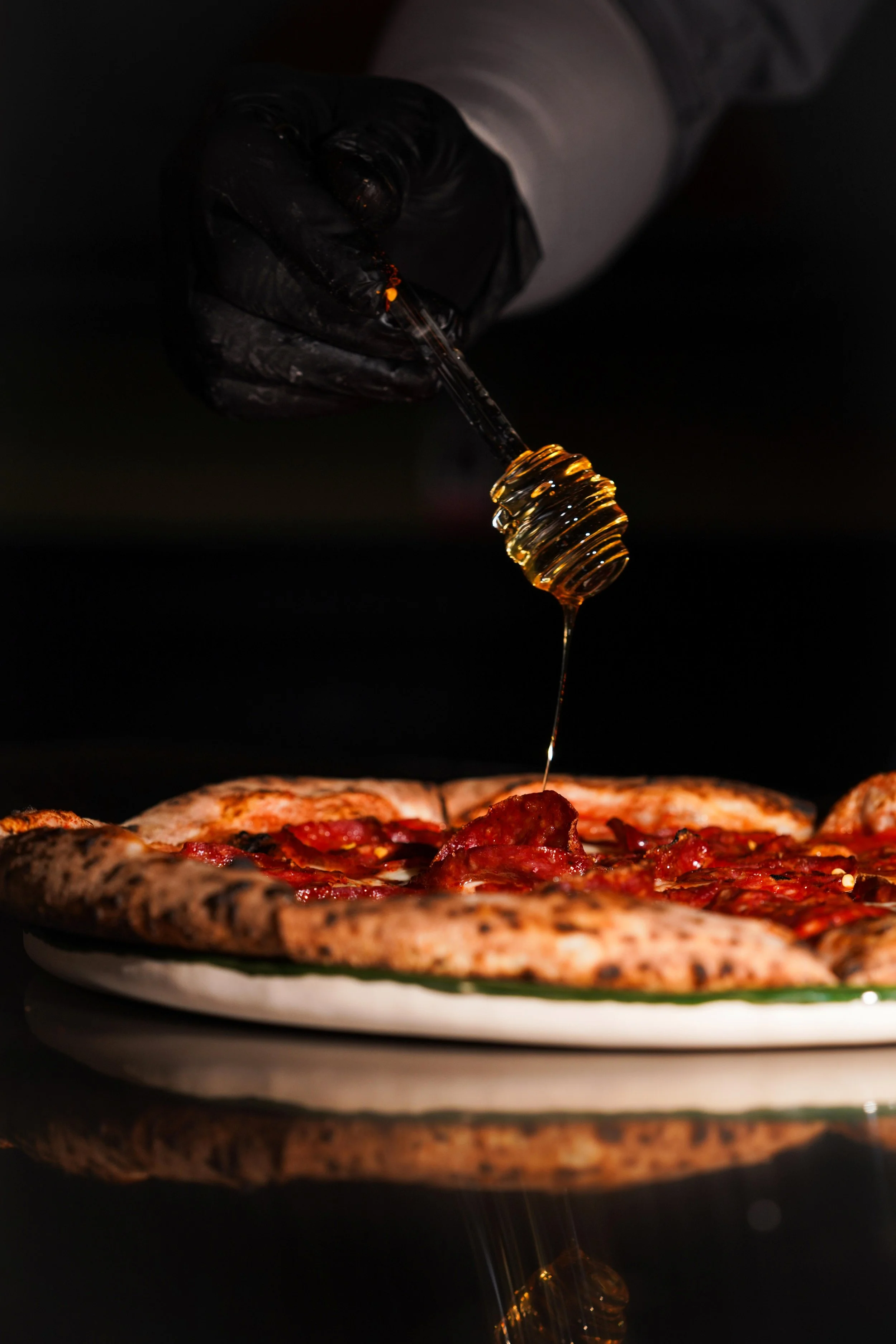 Chef drizzling honey over pepperoni and sausage pizza in a professional kitchen oven.