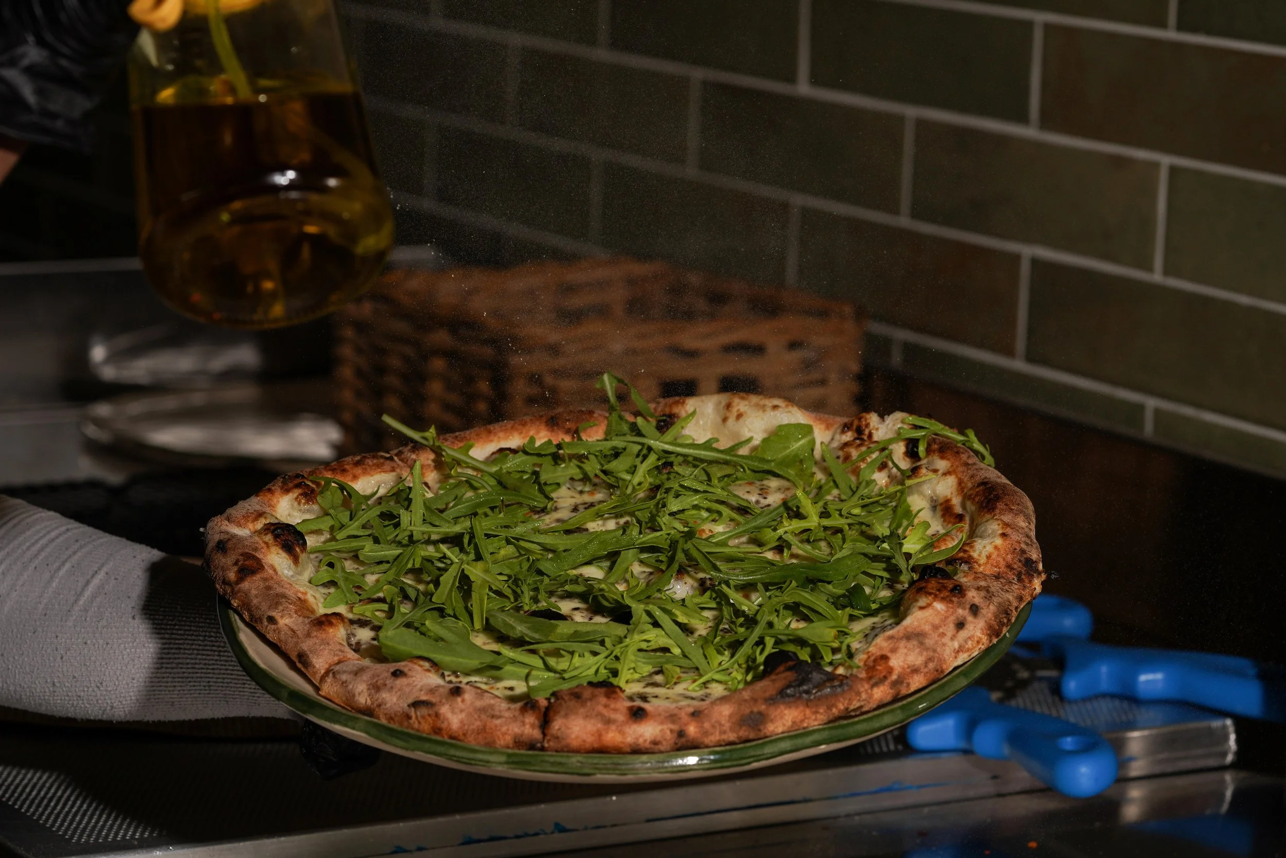 A pizza topped with fresh arugula on a glass plate, being removed from an oven.