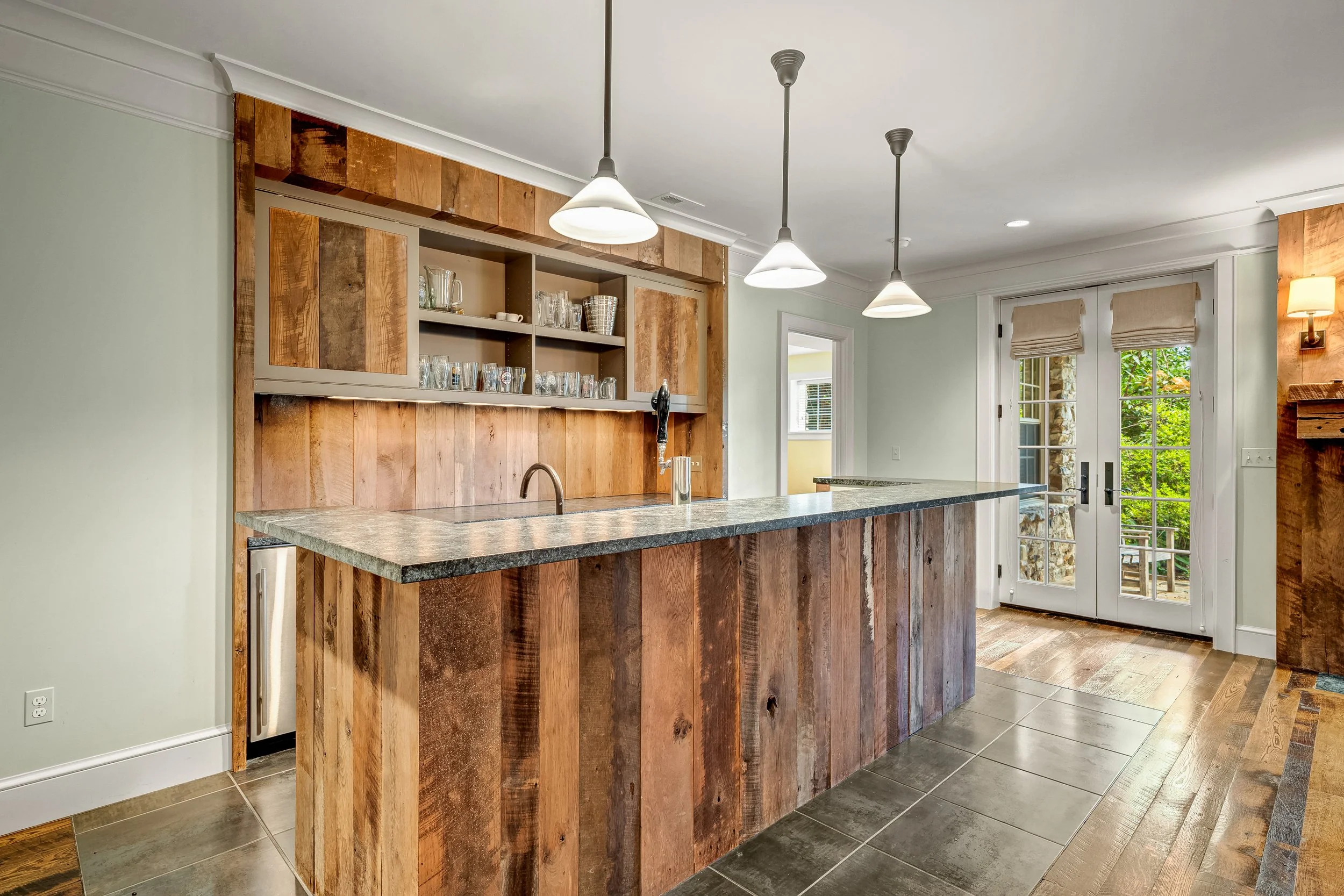 A modern kitchen with a wooden island and open shelving, pendant lights, a granite countertop, and French doors leading outside.