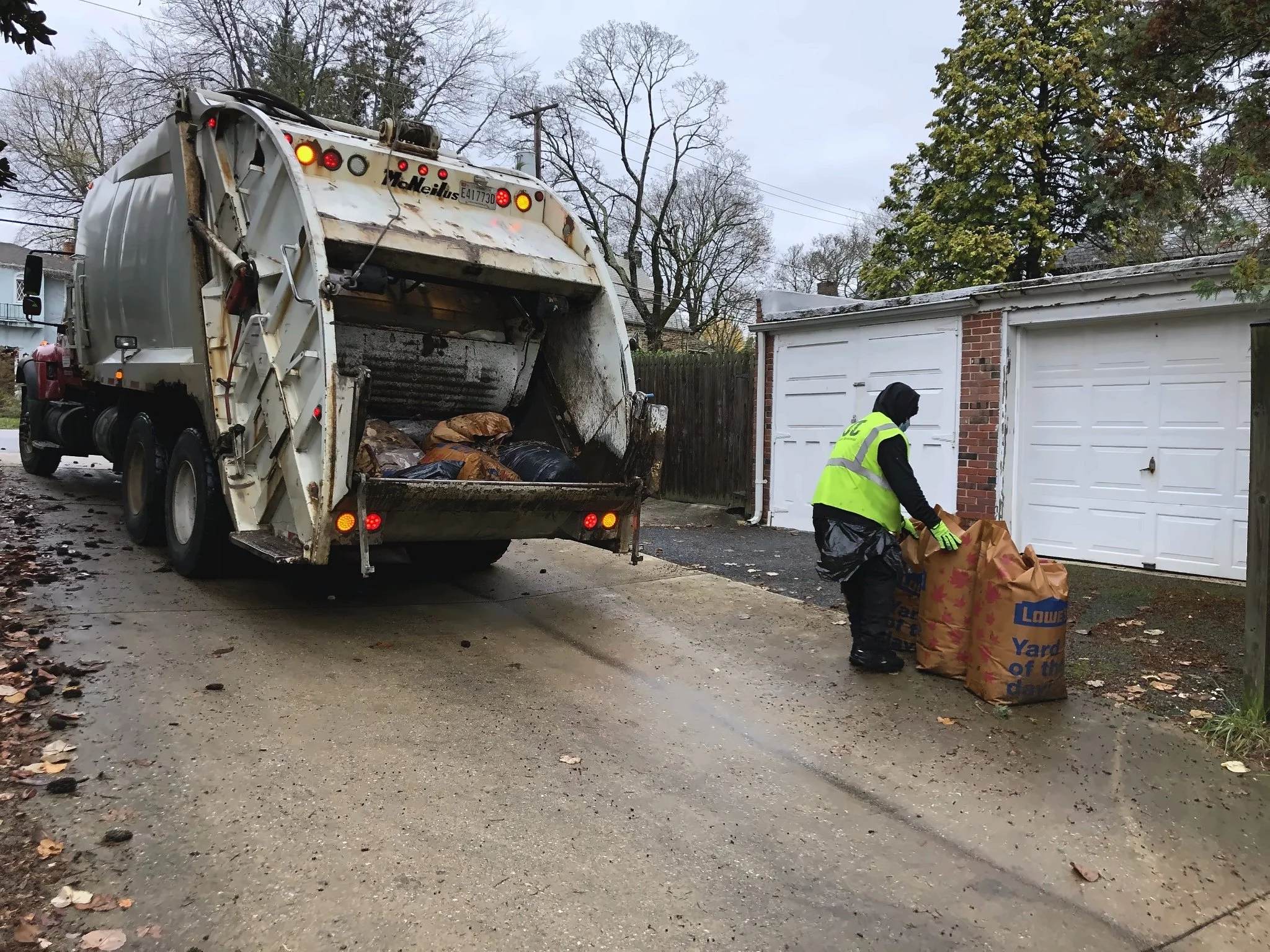 Collection crew loading bags of yard debris into a rear-load truck on a residential street