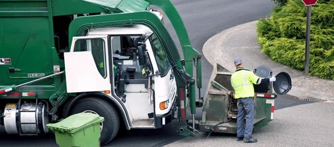 Worker loading a cart into a side-loading garbage truck