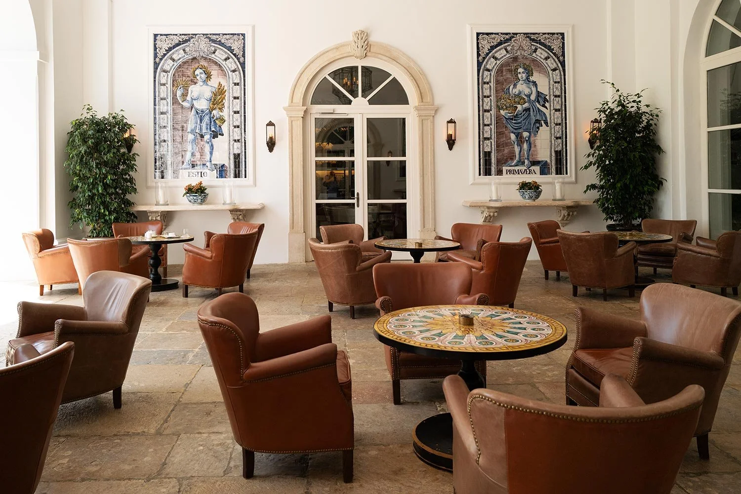 Sunlit courtyard lounge with tan leather armchairs, a mosaic table and Andalusian tile panels.