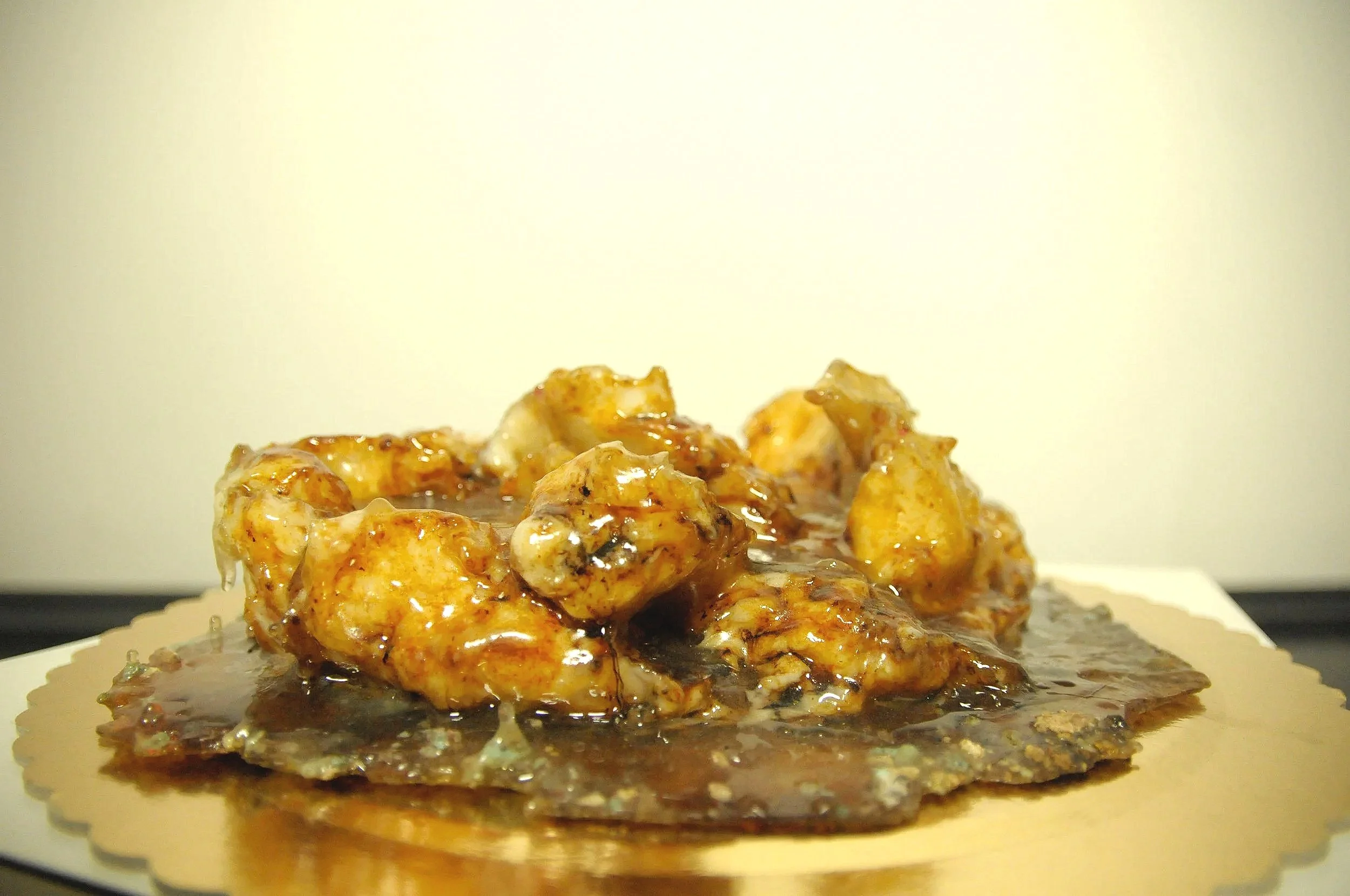 Close-up of a stack of cooked chicken pieces covered in a glossy sauce, placed on a round, textured object that appears to be a stone or cutting board.