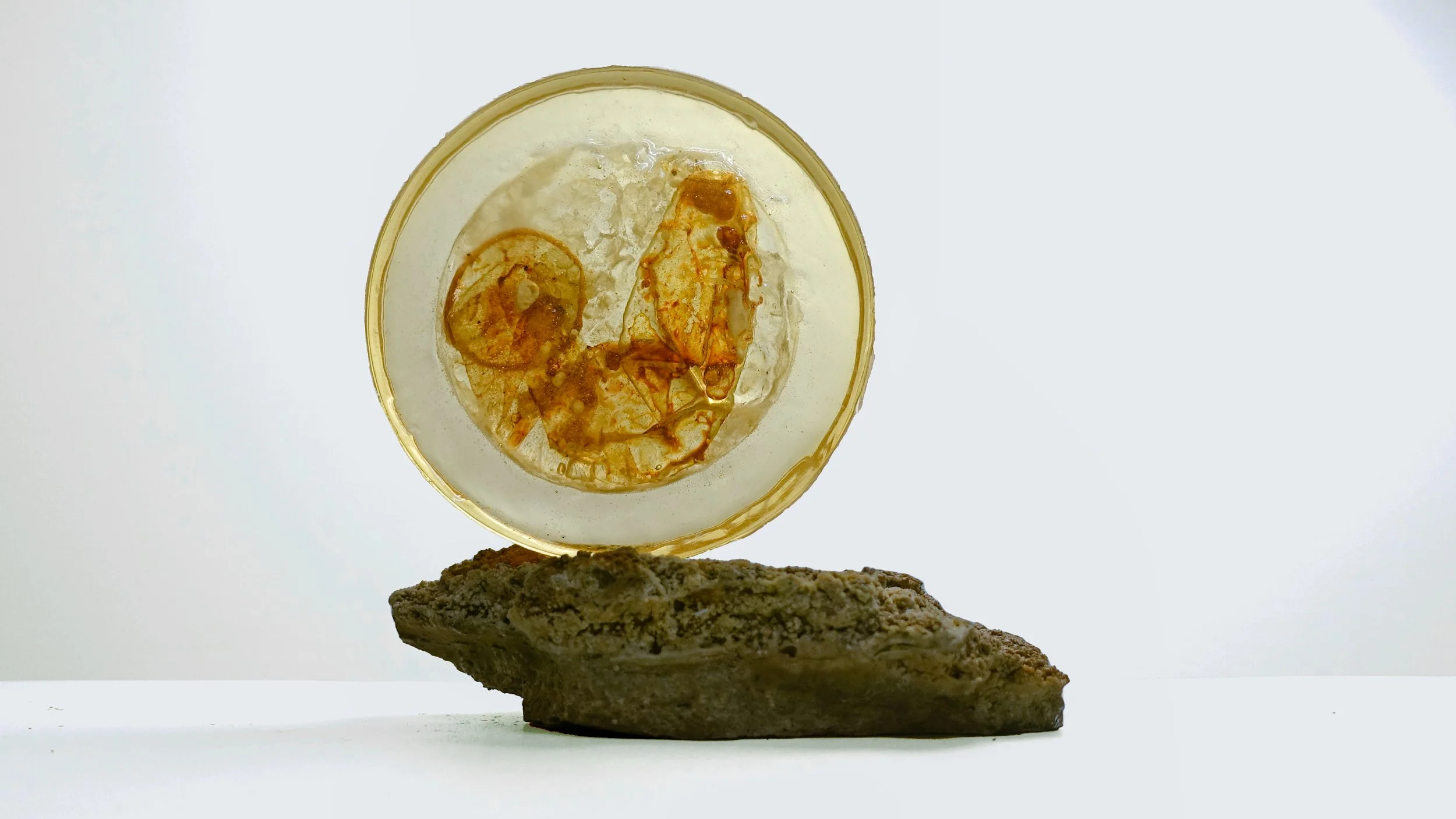 A clear glass with a gold rim holding some lemonade with ice and lemon slices, placed on a piece of rock with a white background.