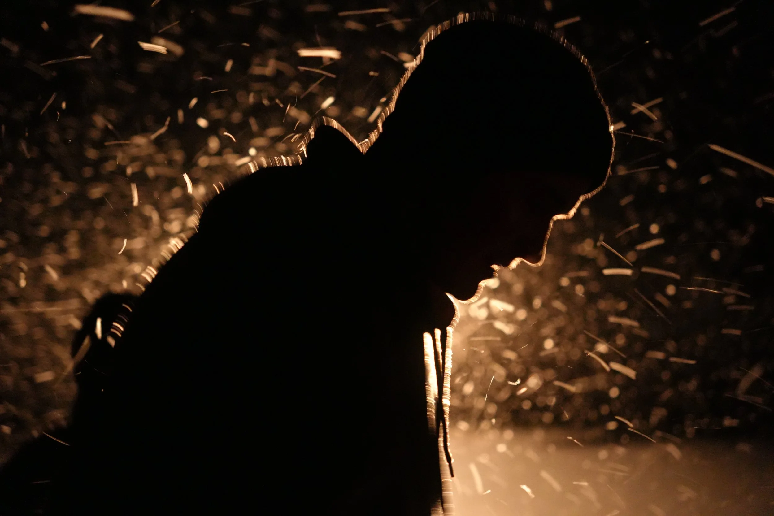 Silhouette of a person at night with light reflecting off water droplets or sparks surrounding them.