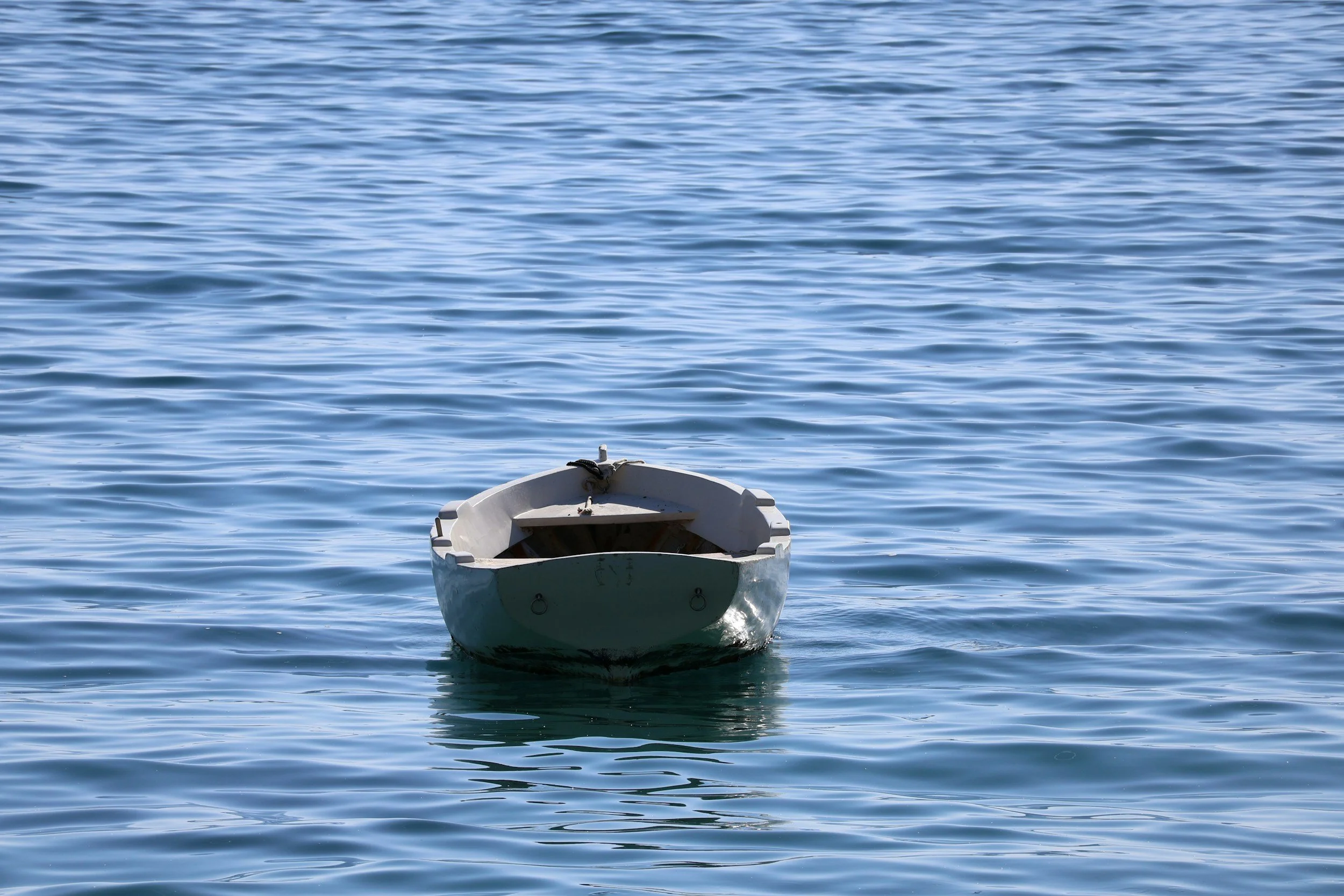 A small white boat floating on calm blue water, with gentle ripples.