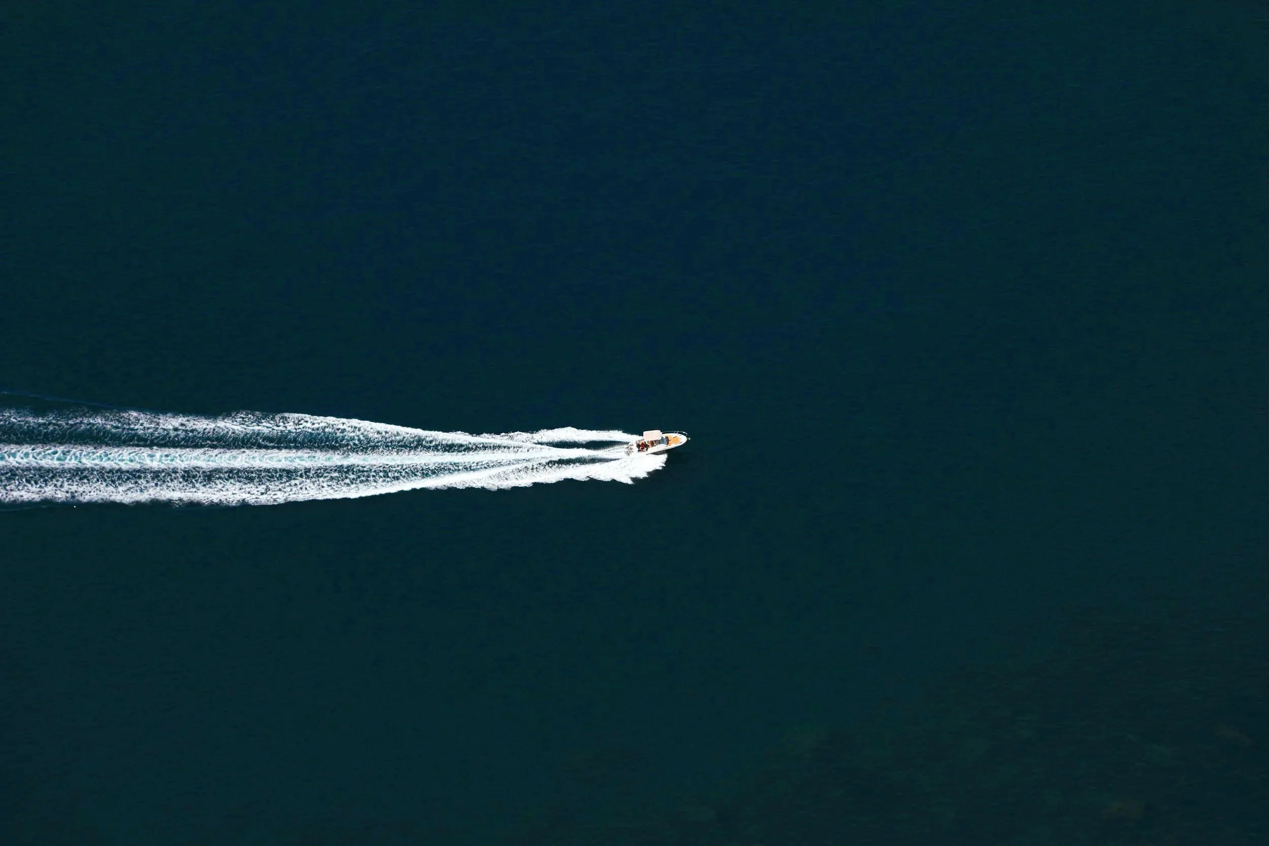 A white motorboat speeding across dark blue water, creating a white wake behind it.