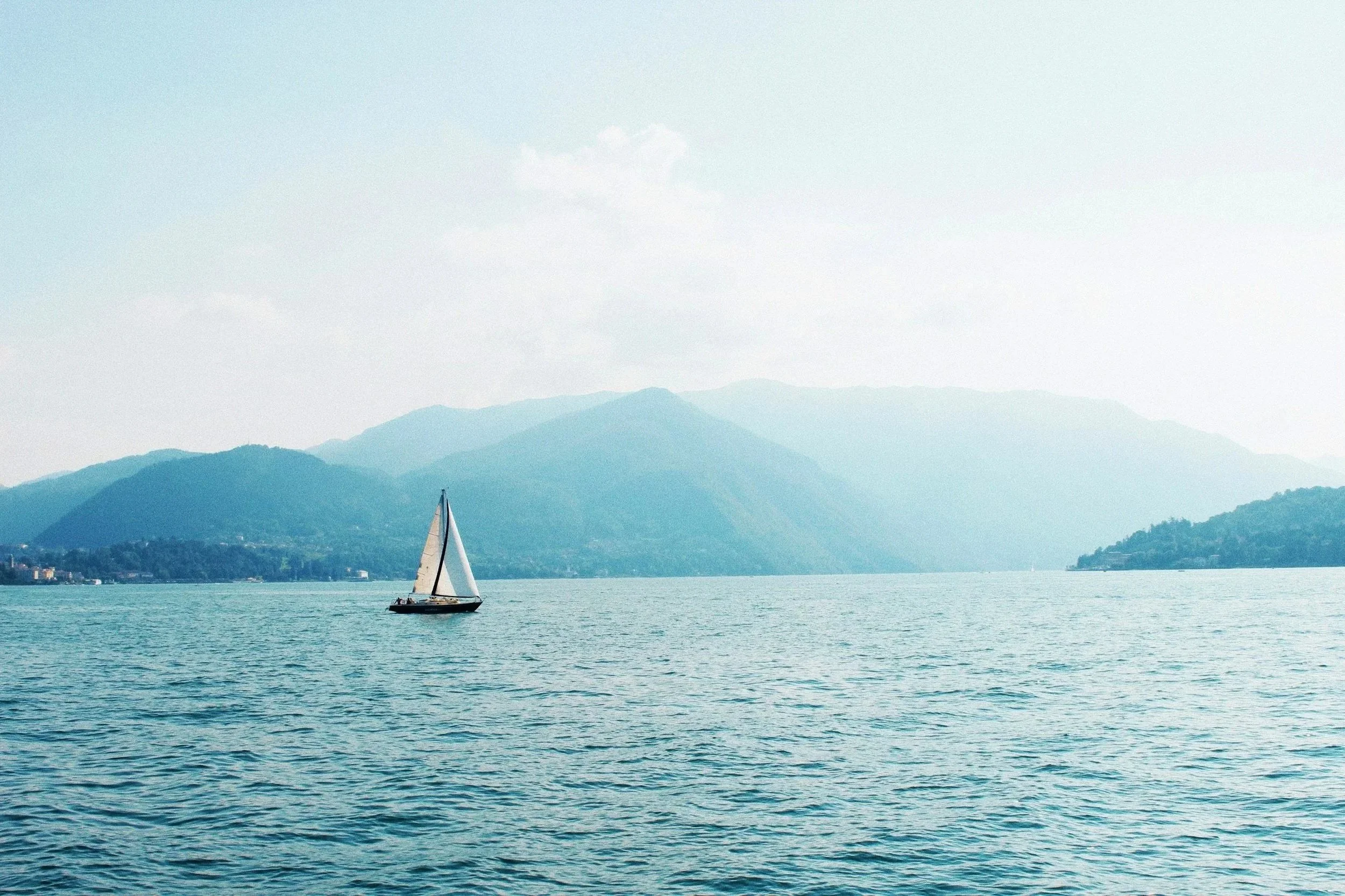 A sailboat on a body of water with mountains in the background and a partly cloudy sky above.