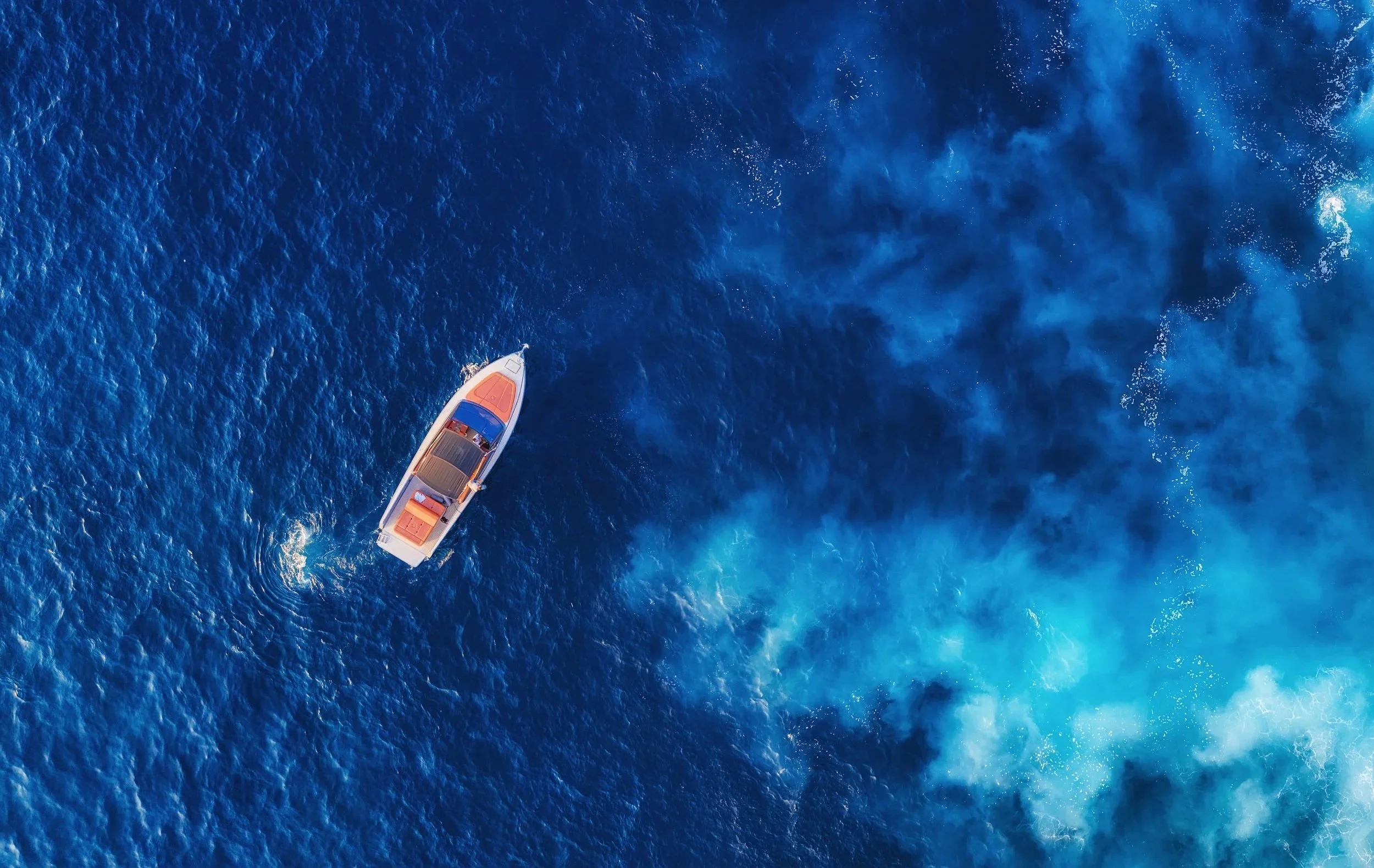 A white motorboat sailing on deep blue ocean water, creating waves and white foam behind it.