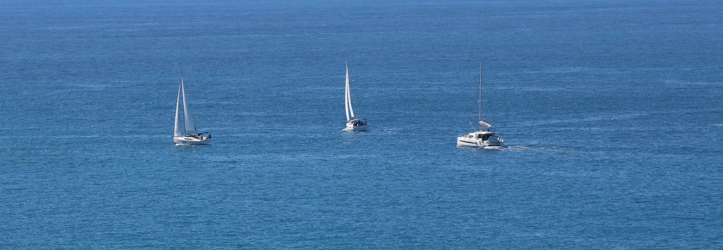 Three sailboats and one motorboat on calm blue water