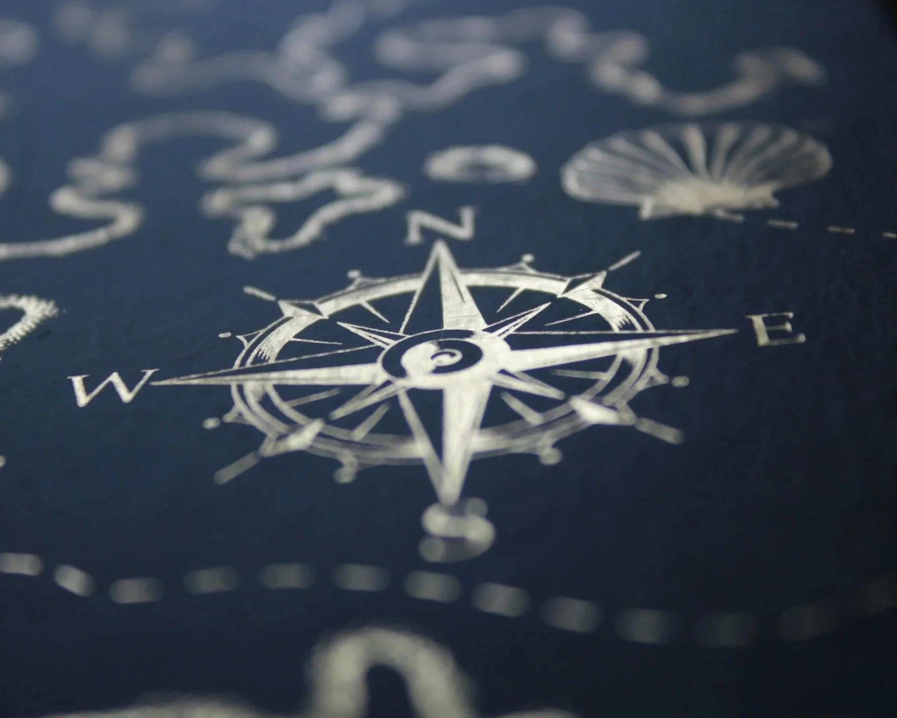Close-up of a metallic compass rose design on a dark surface with starfish and abstract coral patterns in the background.