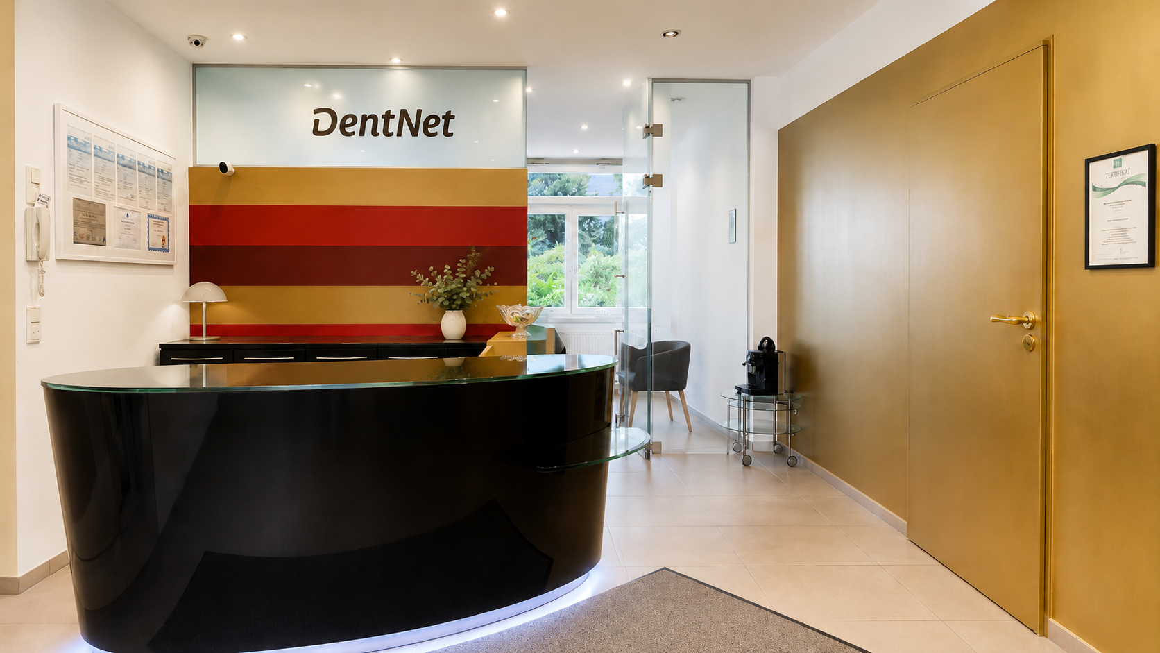 Rezeption in einer Zahnarztpraxis mit schwarzer Theke, Wand mit Firmenname 'DentNet', Fenster mit Blick ins Grüne, Goldene Wand, eingerichtete Ecke mit Kaffeemaschine.