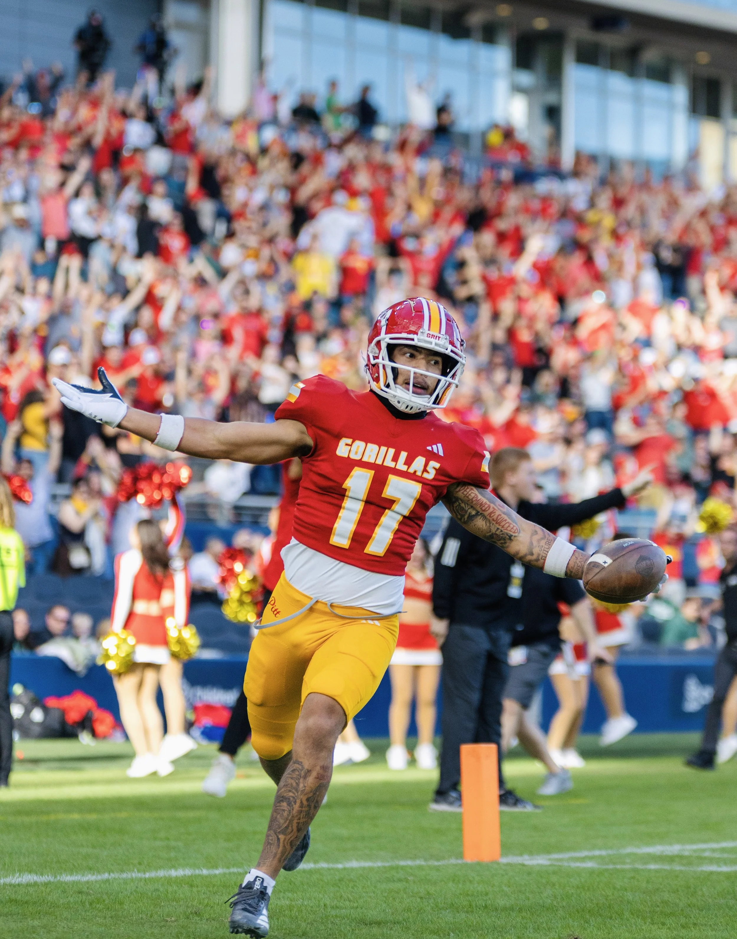 A football player in a red and yellow uniform with the number 15 is running with the football on the field during a game with a crowd of spectators in the background.