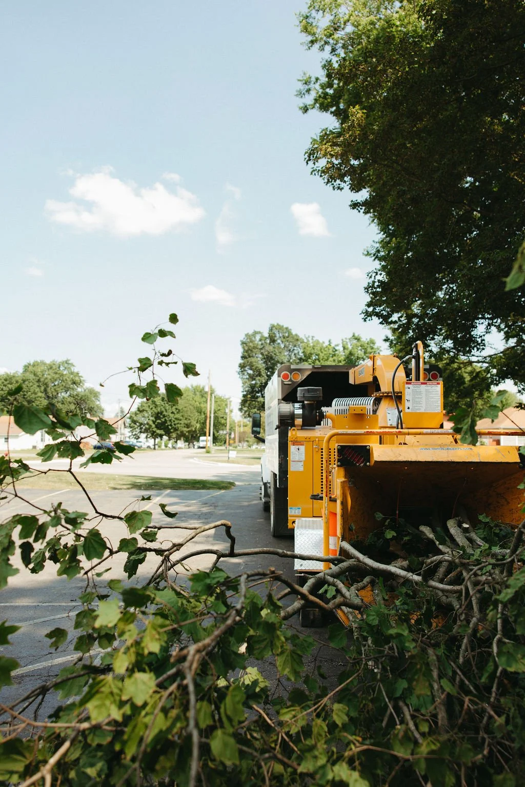 A street sweeper clearing fallen tree branches from a parking lot under a clear blue sky.
