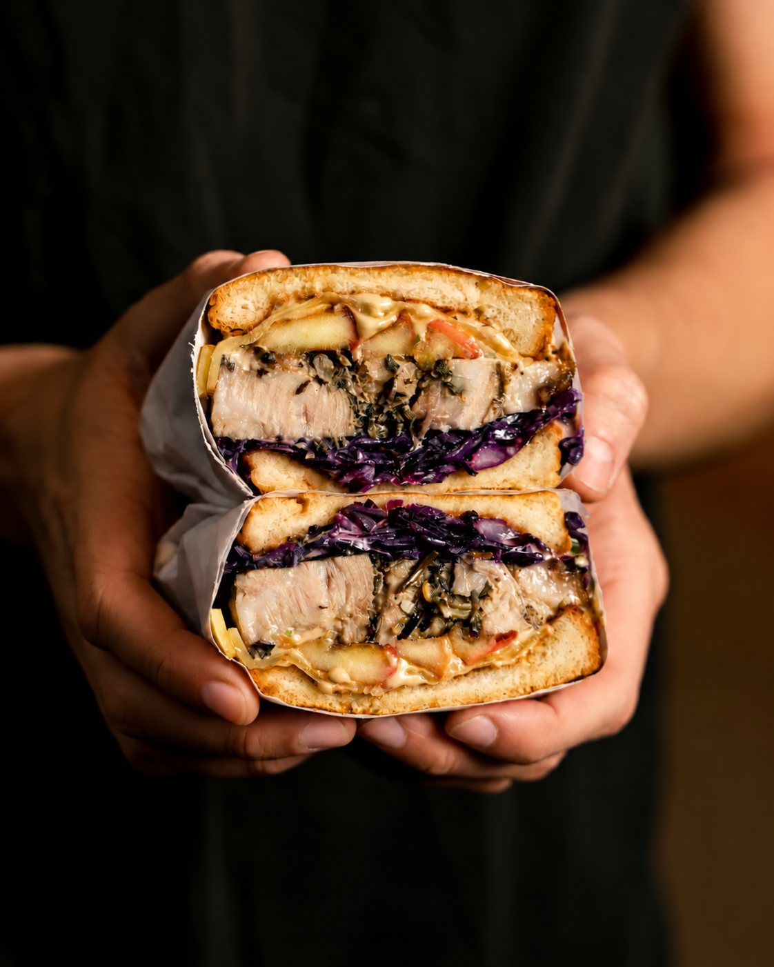 A halved evening wedding sandwich filled with pulled meat and red cabbage, held in two hands.