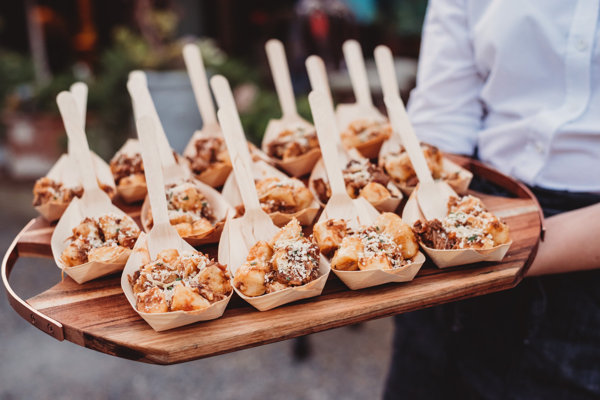 A wooden tray of evening wedding food, loaded fries served in paper boats with wooden forks.