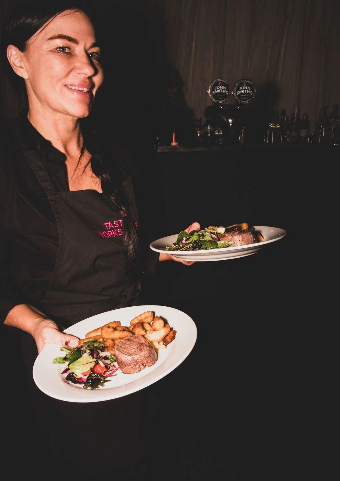Taste Cuisine team member carrying two plates of fillet steak with chips and salad