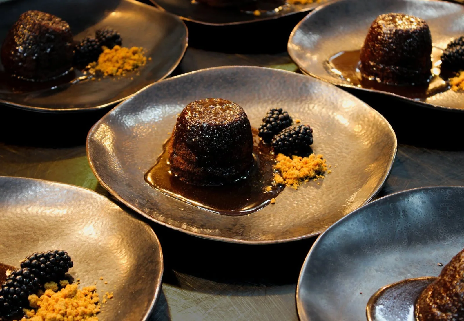 Sticky toffee pudding with blackberries and honeycomb on a dark ceramic plate