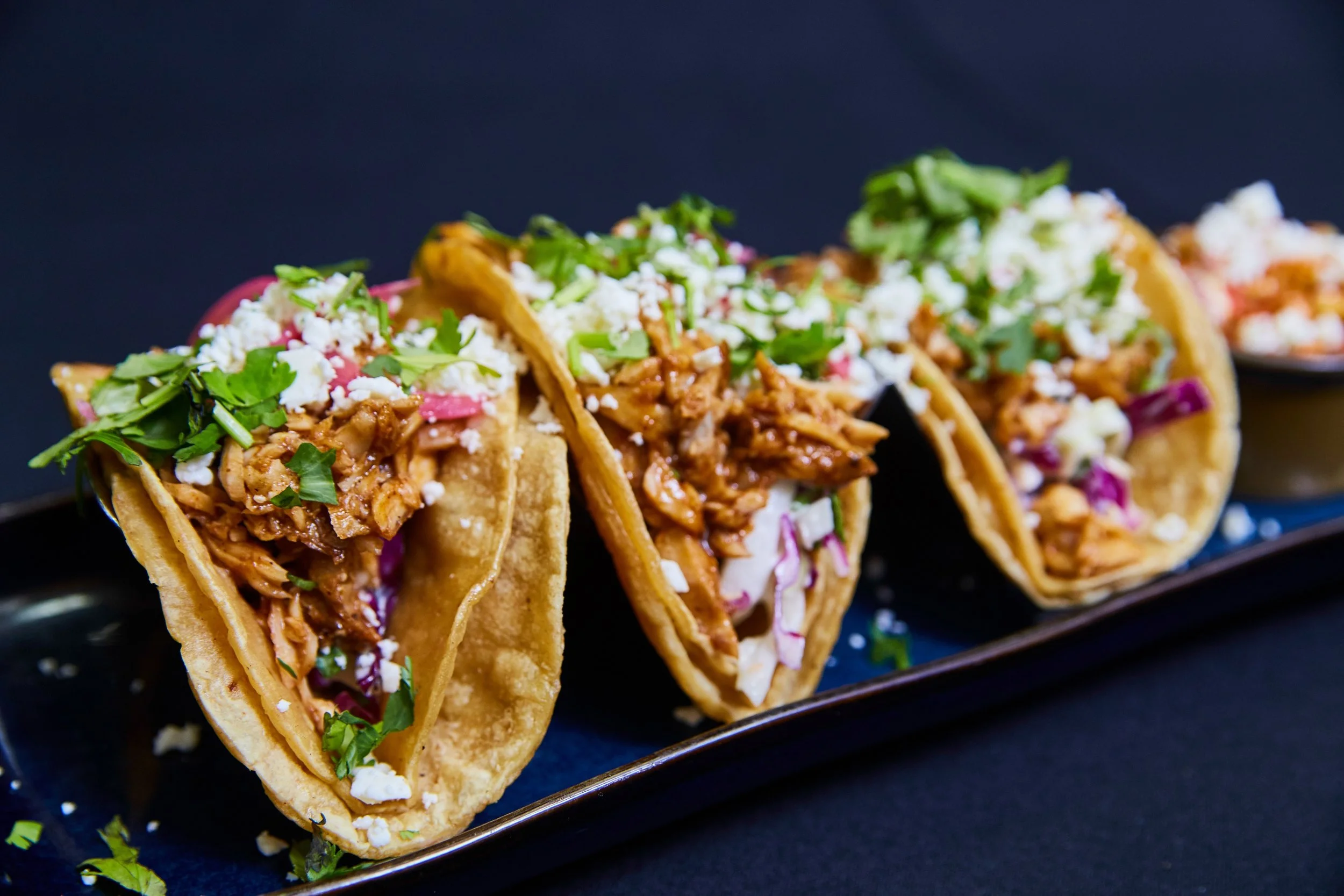 Three loaded tacos with pulled meat, pickled red onion, crumbled cheese and fresh coriander.