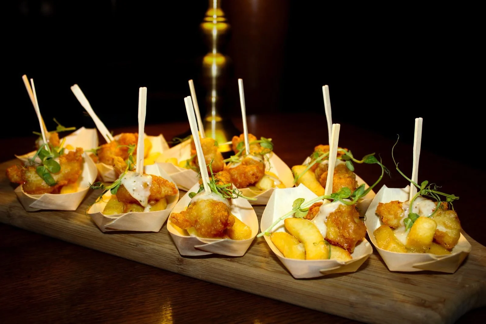 Mini fish and chips canapés served on a wooden board with skewers