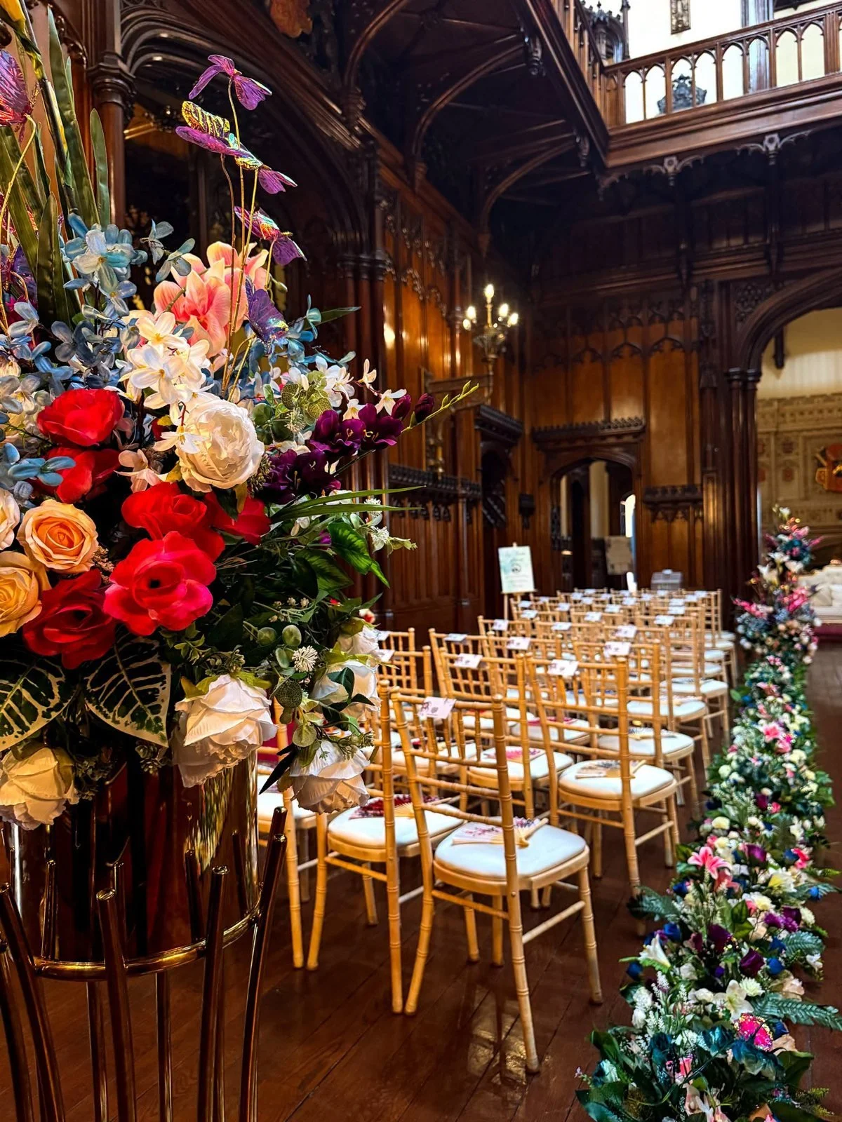 Colourful ceremony flowers beside gold chairs in the Great Hall at Allerton Castle