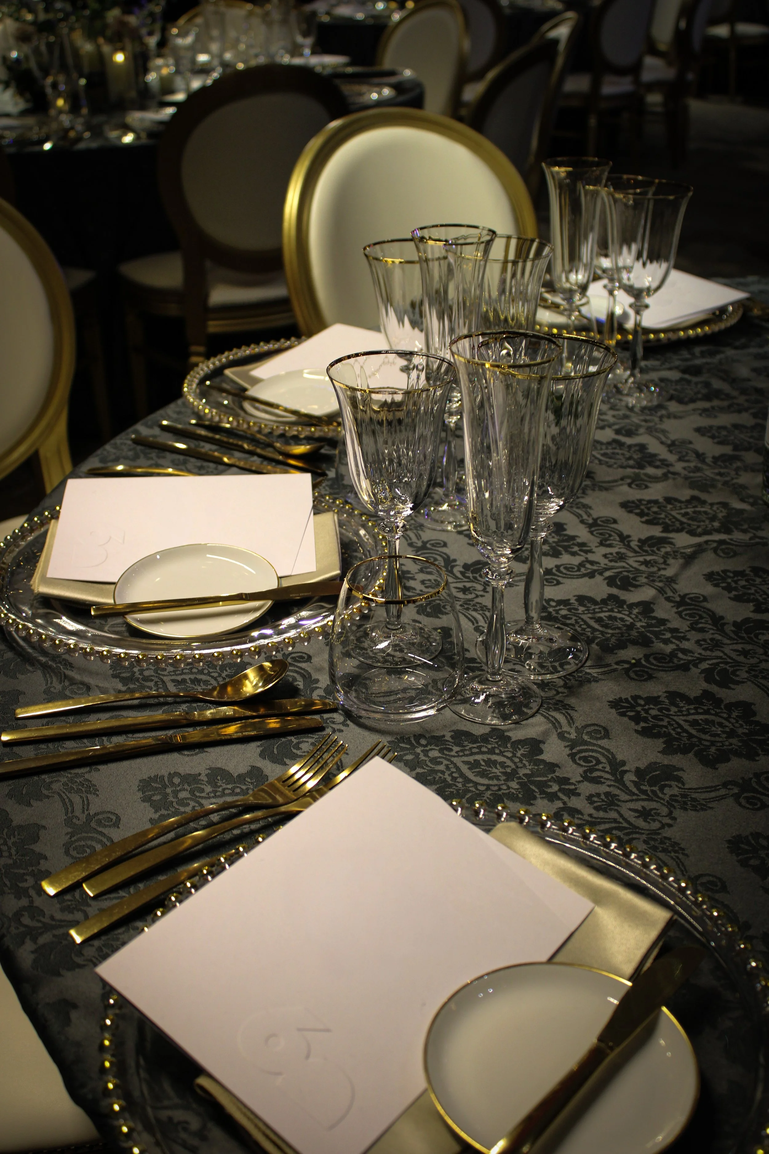 Corporate event catering: an elegantly laid table with gold-rimmed glassware, napkins and cutlery on dark damask linen.