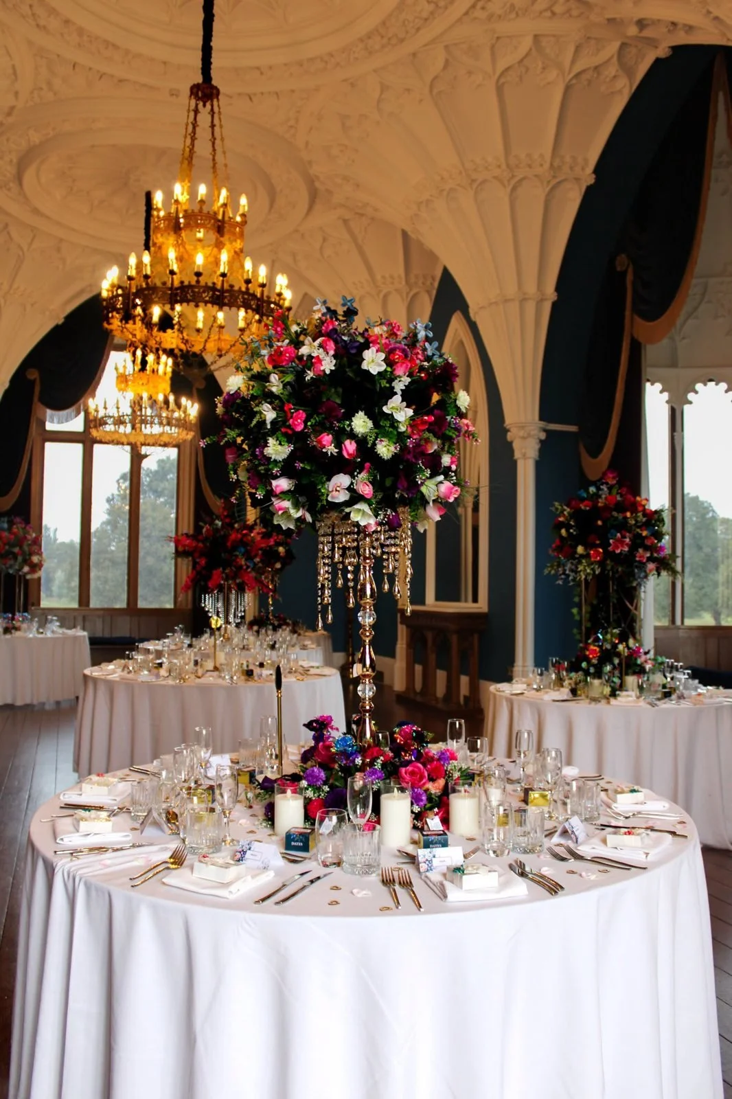 Round wedding table with a tall floral centrepiece under a chandelier