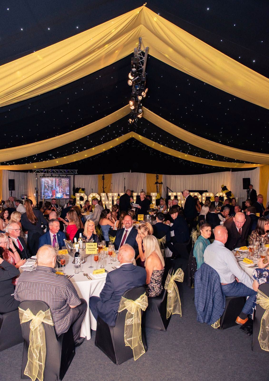 Starlit marquee ceiling with yellow drapes above guests at round tables