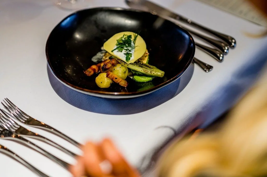 Plated vegetable starter with baby potatoes, charred greens and fresh herbs in a black bowl on a wedding table