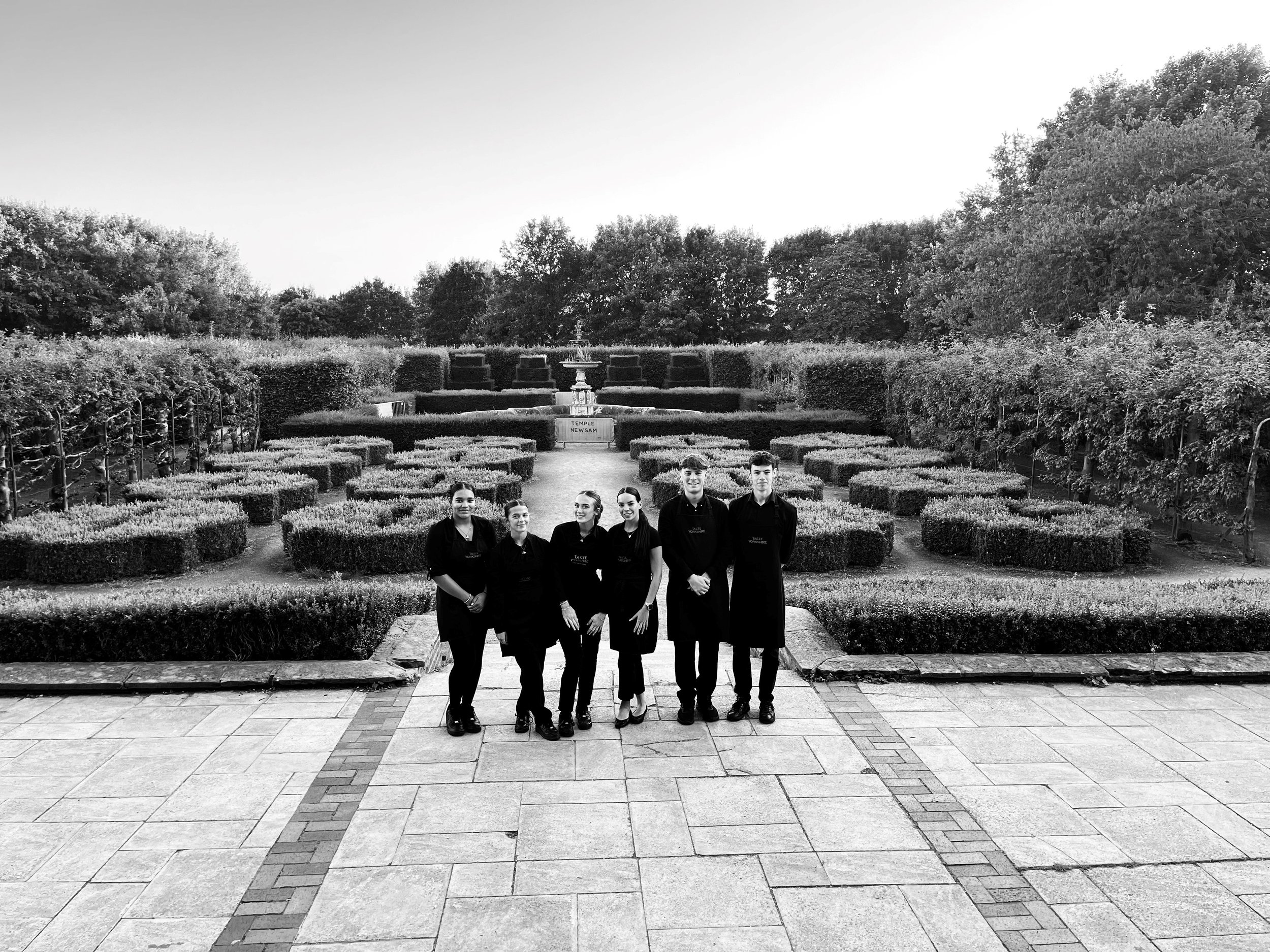 Black and white photo of a formal country house garden with clipped hedges and a central fountain.