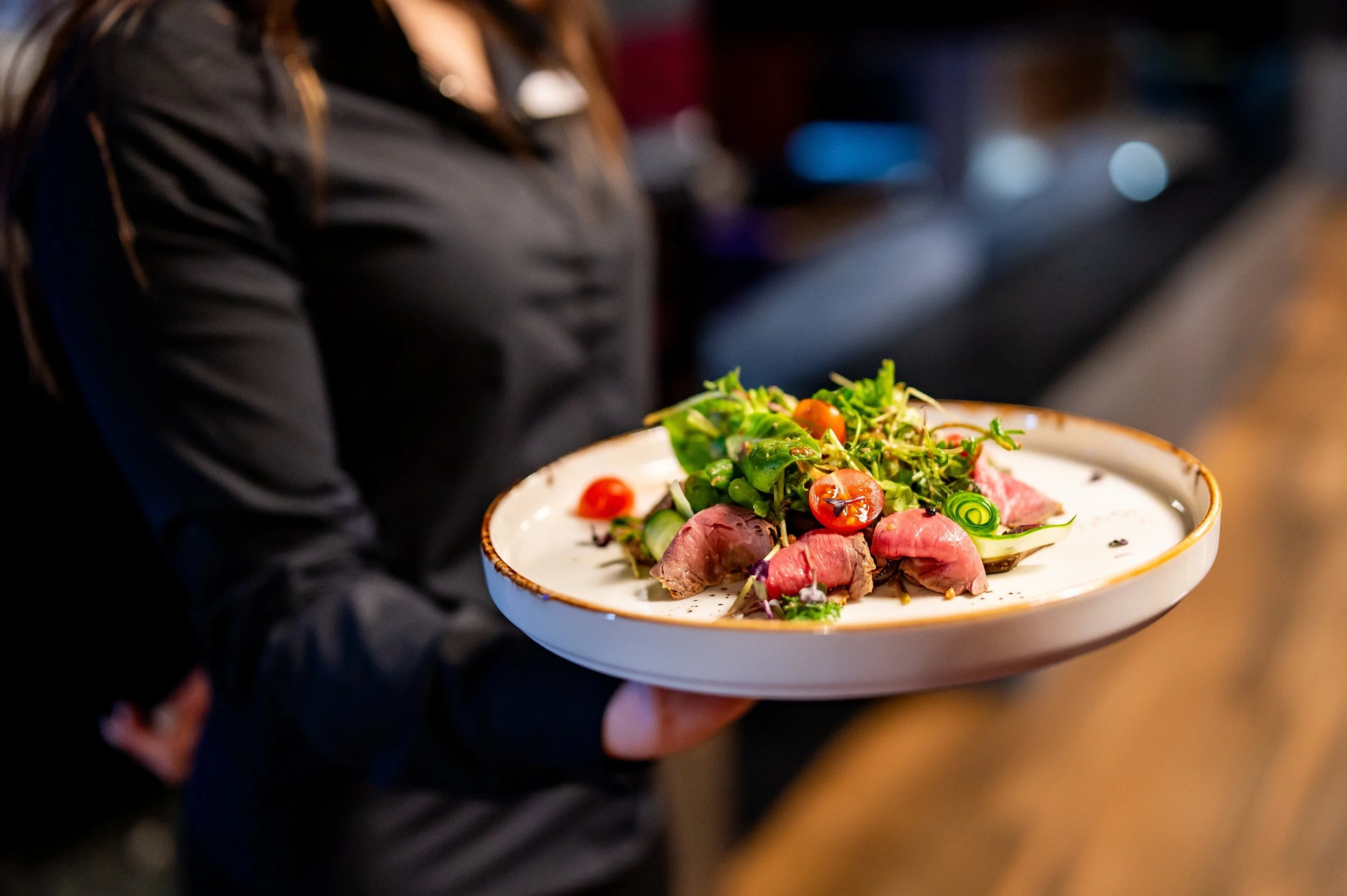 A waiter presenting a beautifully plated beef dish with fresh salad garnish, served on a white plate at a Taste Cuisine event.