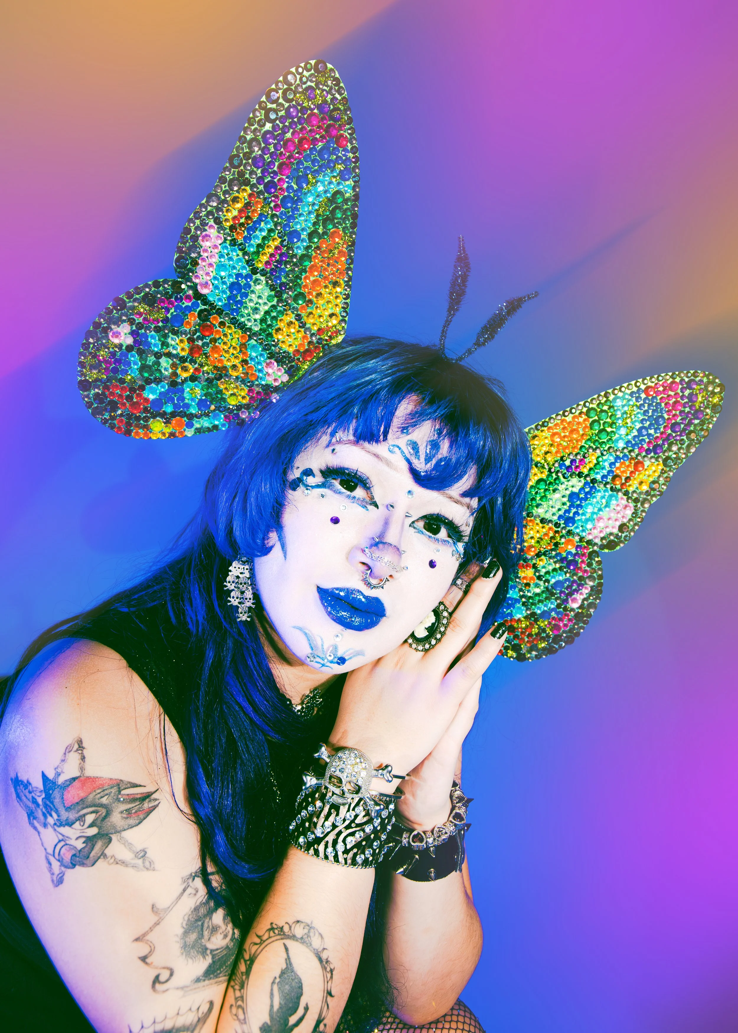Local Dallas, Texas, DFW Non-traditional Fashion Editorial Creative Portraits Cover Art Photographer Photoshoot. A woman with blue hair and tattoos, dressed in dark clothing, wearing colorful rhinestone butterfly ear headbands and jewelry, posing aga