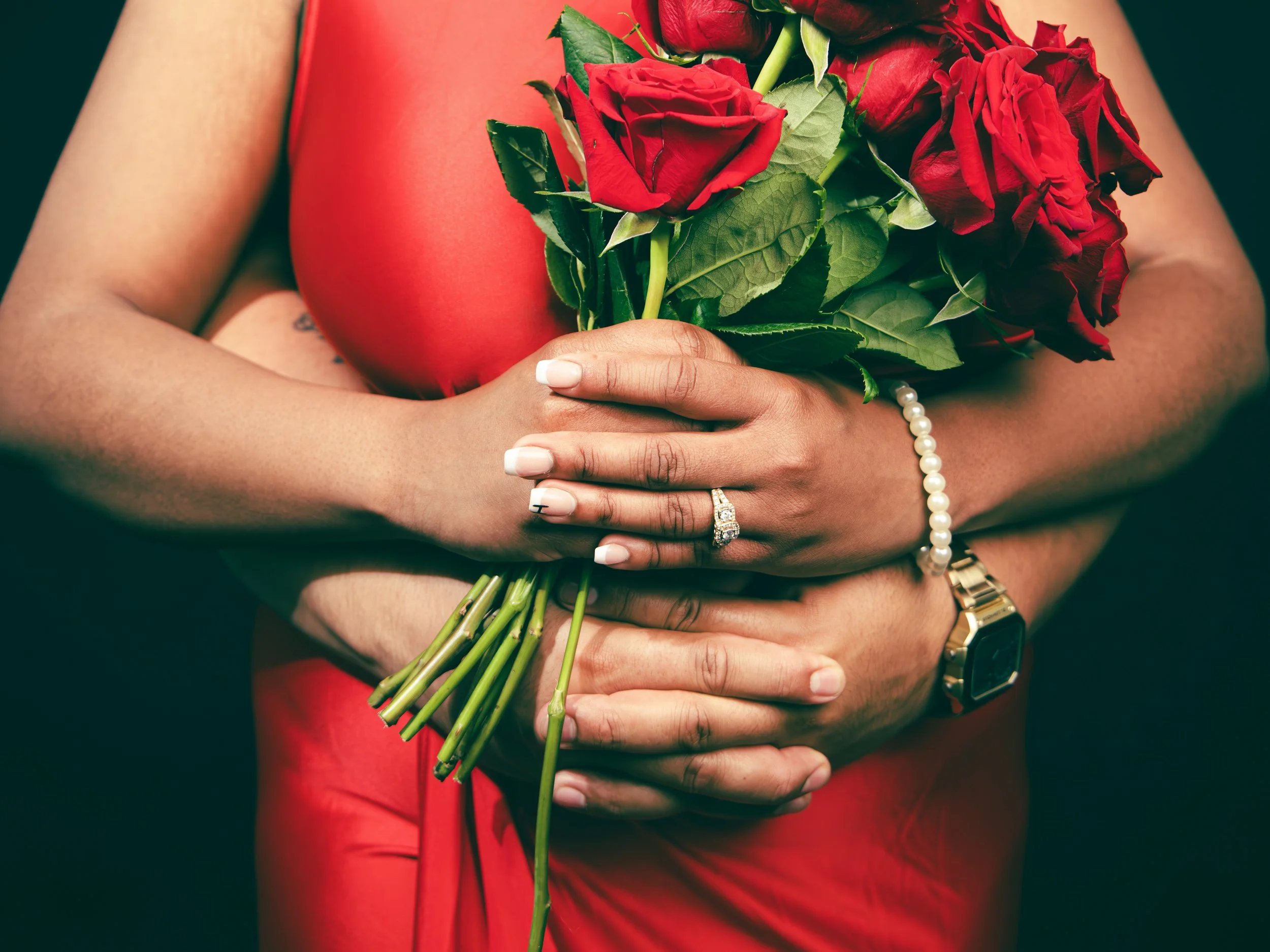 Local Dallas, Texas, DFW Non-traditional Fashion Editorial Creative Portraits Cover Art Photographer Photoshoot. A person wearing a red dress holding a bouquet of red roses with green leaves, wearing a pearl bracelet, a gold watch, and an engagement 